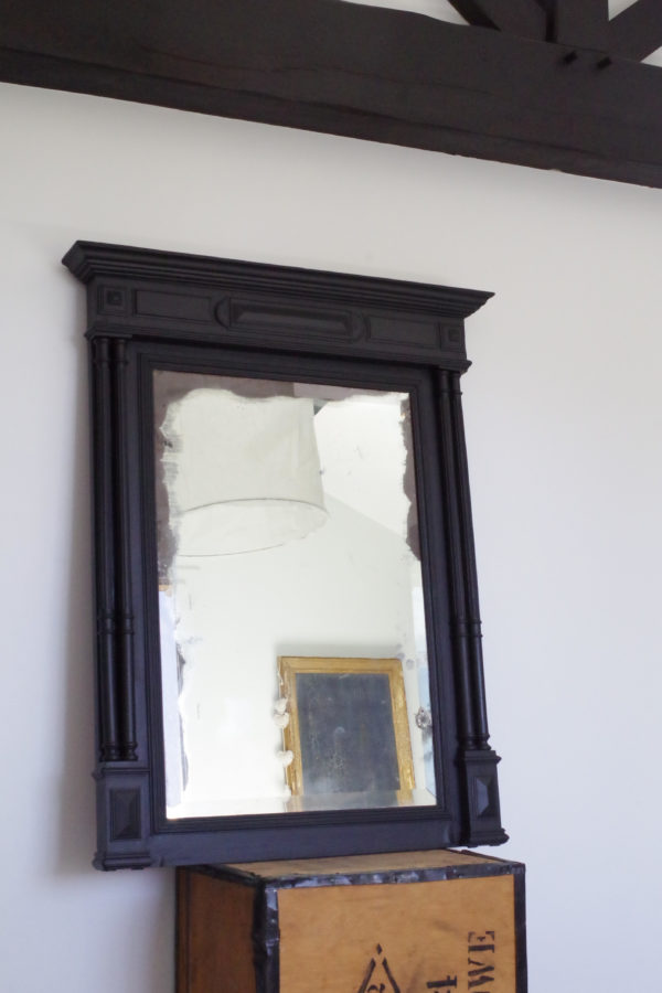 Ce miroir ancien en bois sculpté est mercurisé et son tain est largement patiné sur les pourtours.