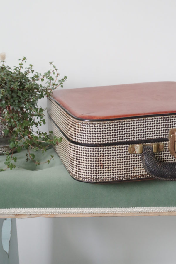 Cette petite valise ancienne est en carton bouilli protégé par un revêtement en vinyle aux motifs pieds-de-poule noirs et blancs.