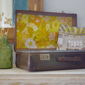 Datant des années 50-60, cette valise vintage en fibre vulcanisée dégage un charme rétro indéniable avec son intérieur tapissé d'un papier peint vintage.