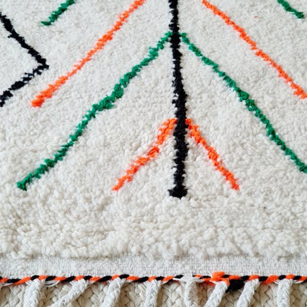 Ce tapis berbère affiche une trame écrue avec de chouettes lignes géométriques noires, vertes et oranges fluo pour pièce résolument décalée