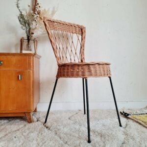 Chaise en rotin vintage juchée sur un piétement en métal noir fuselé