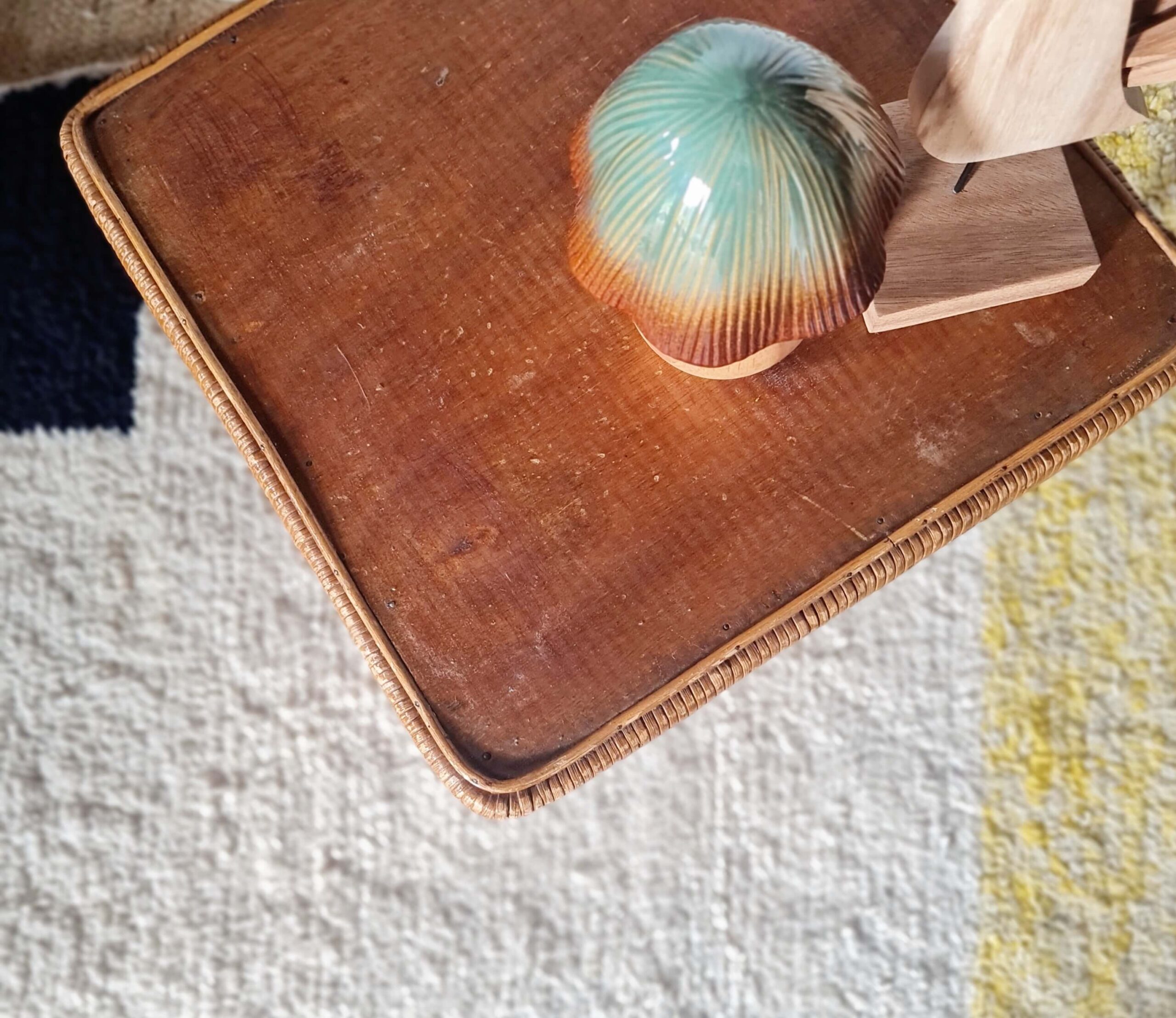 Vue du dessus d'une petite table vintage montrant son plateau en bois verni ceinturé de rotin tressé, avec une figurine de champignon en céramique.