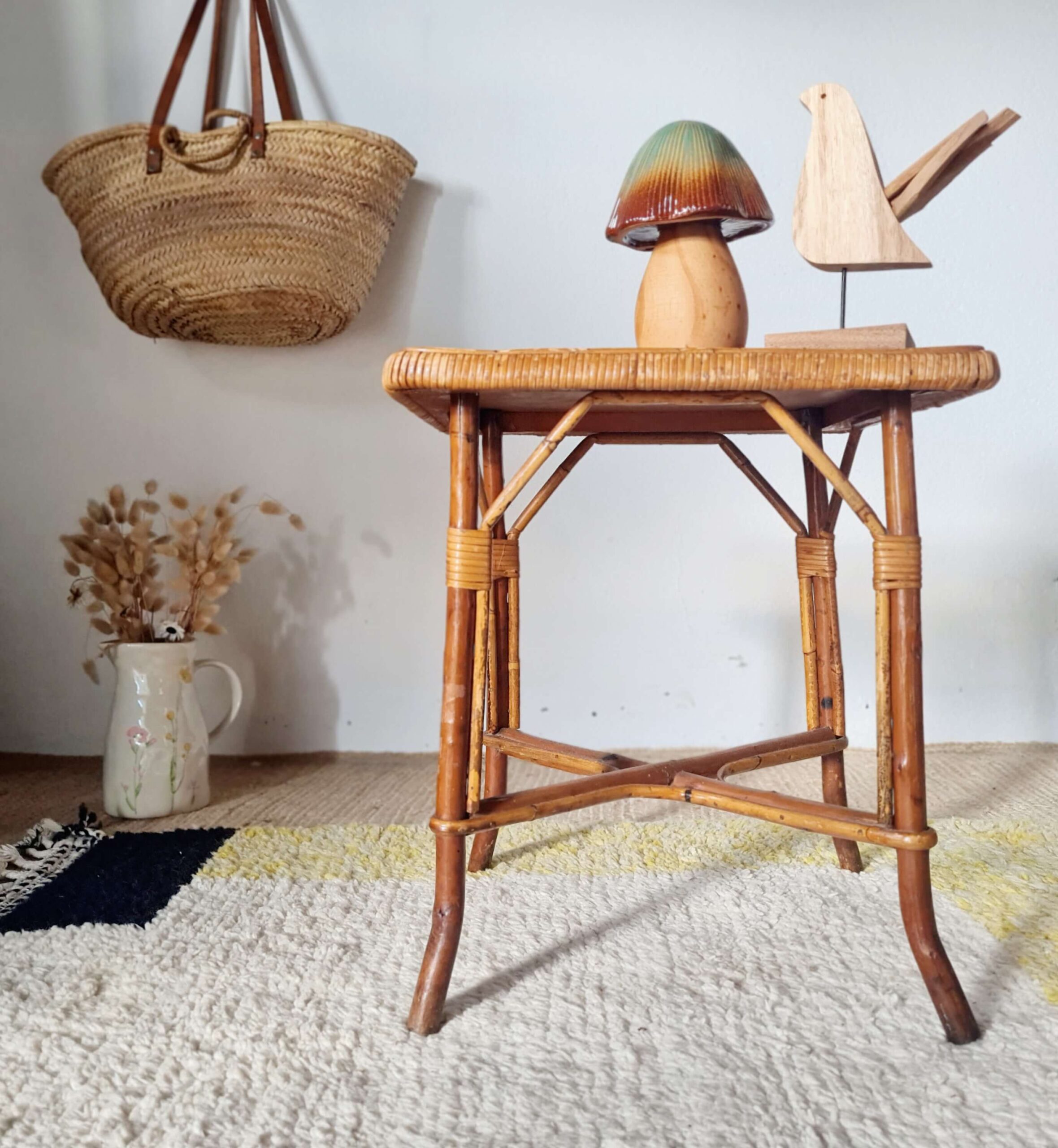 Plan rapproché sur le profil d'une sellette vintage, montrant l'assemblage artisanal des tiges de rotin et les finitions nouées sous le plateau.