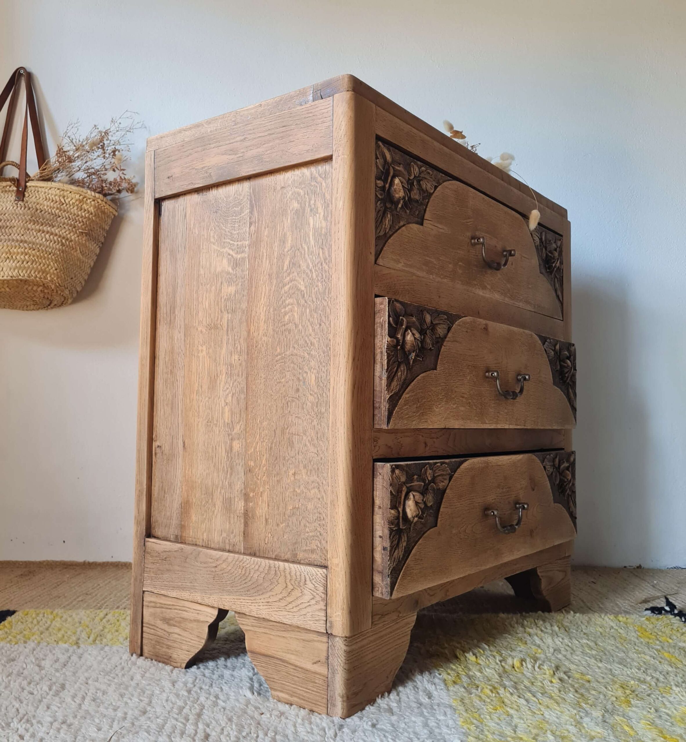 Vue d'ensemble de l'arrière de la commode ancienne montrant sa structure saine. Le panneau de fond est en bois de teinte rousse, encadré par le montant robuste et foncé du meuble d'origine. Un panier en osier est visible en arrière-plan à gauche.