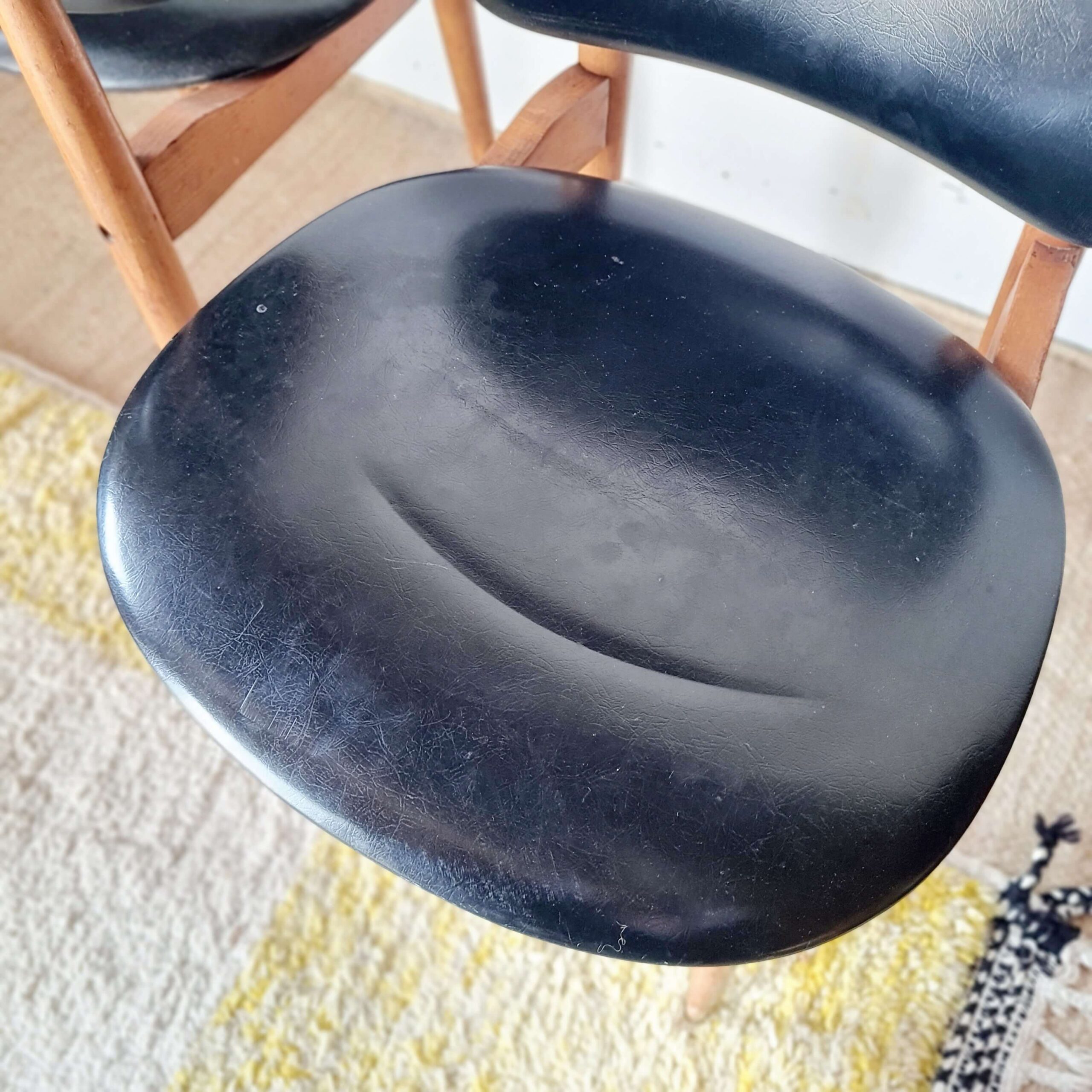 Gros plan plongeant sur l'assise en skaï noir mat d'une chaise vintage, montrant le grain du vinyle et sa patine d'origine
