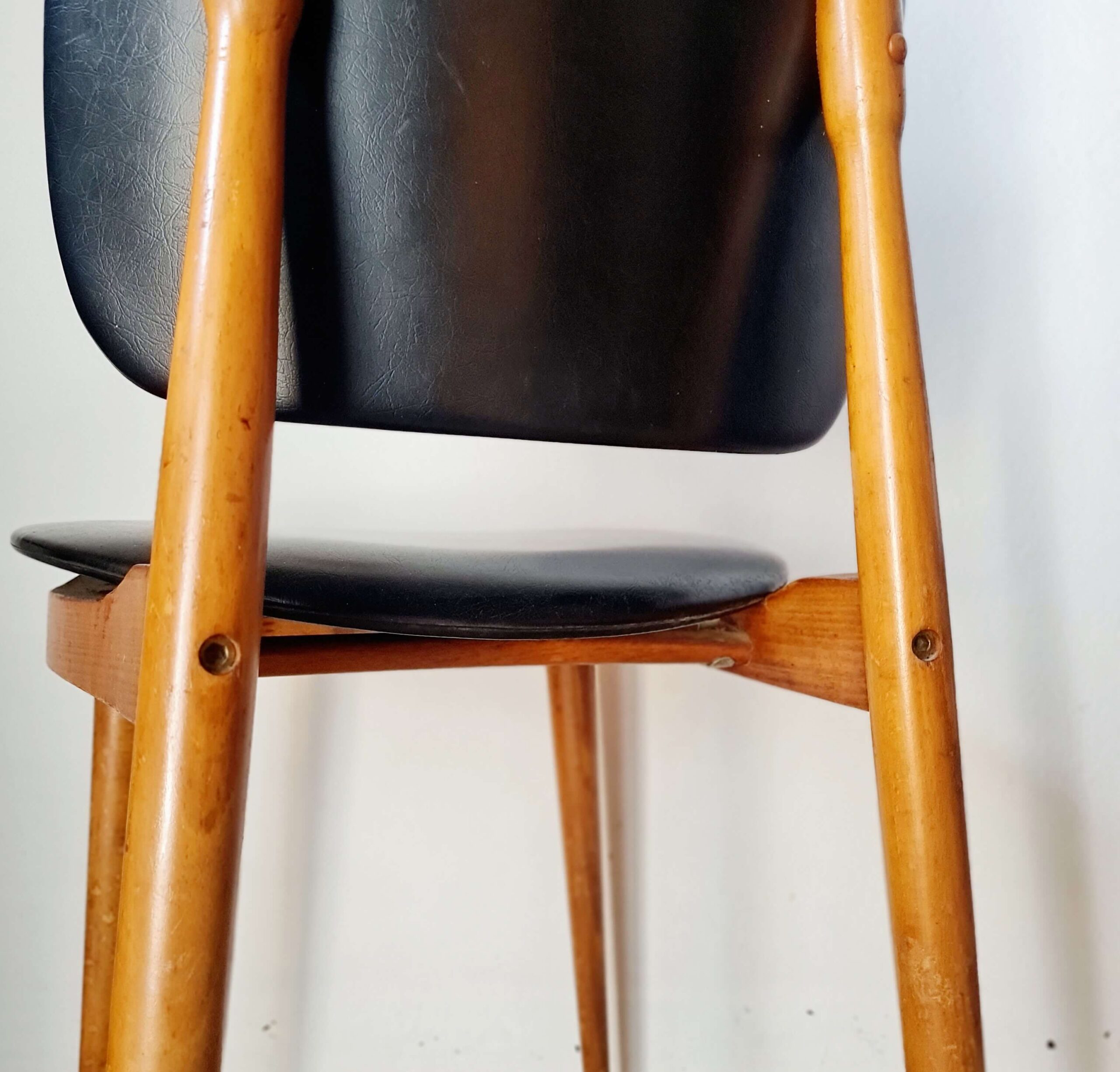 Vue rapprochée de la structure inférieure d'une chaise scandinave des années 60, mettant en valeur l'assemblage en bois clair verni et ledessous de l'assise noire.