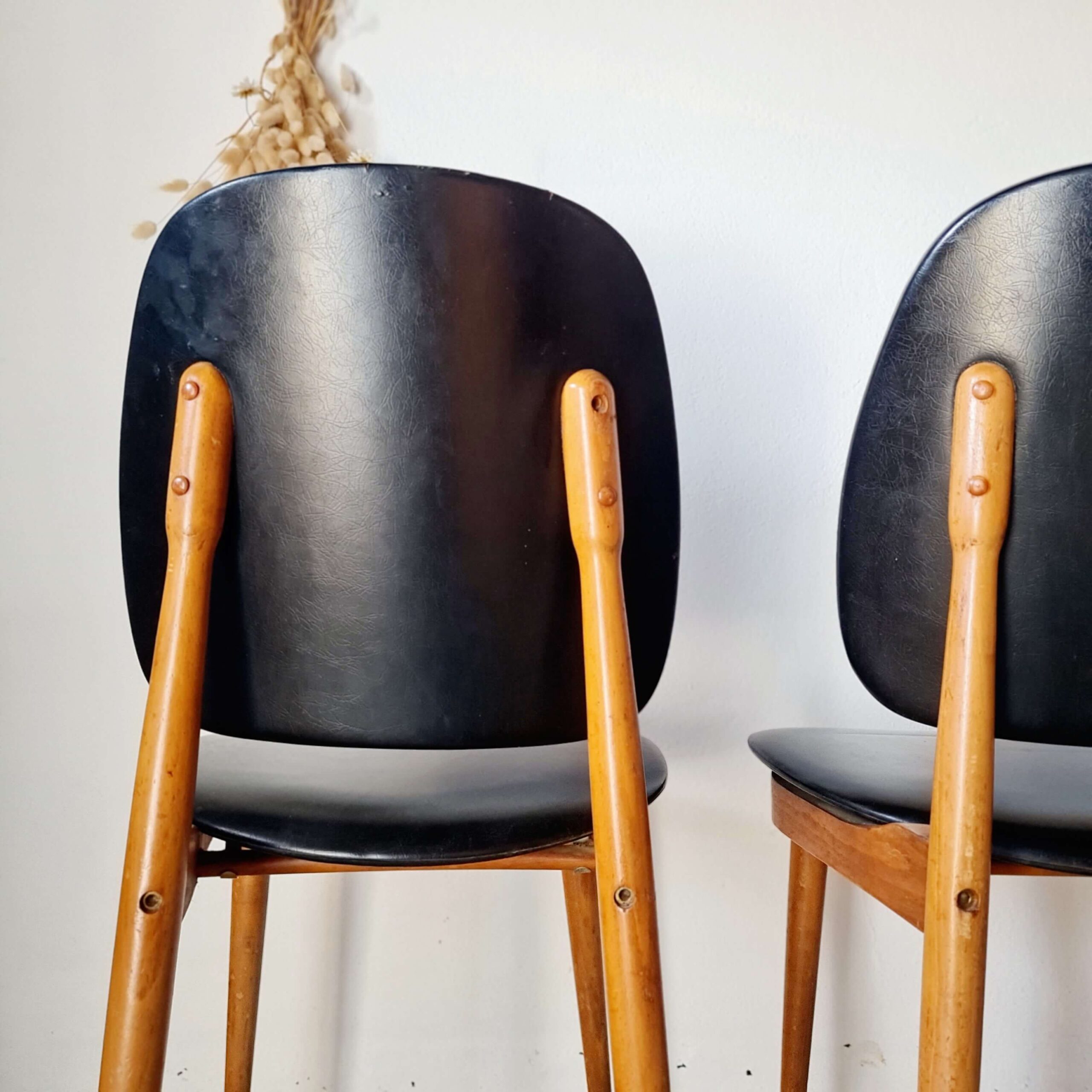 Gros plan plongeant sur l'assise en skaï noir mat d'une chaise vintage, montrant le grain du vinyle et sa patine d'origine