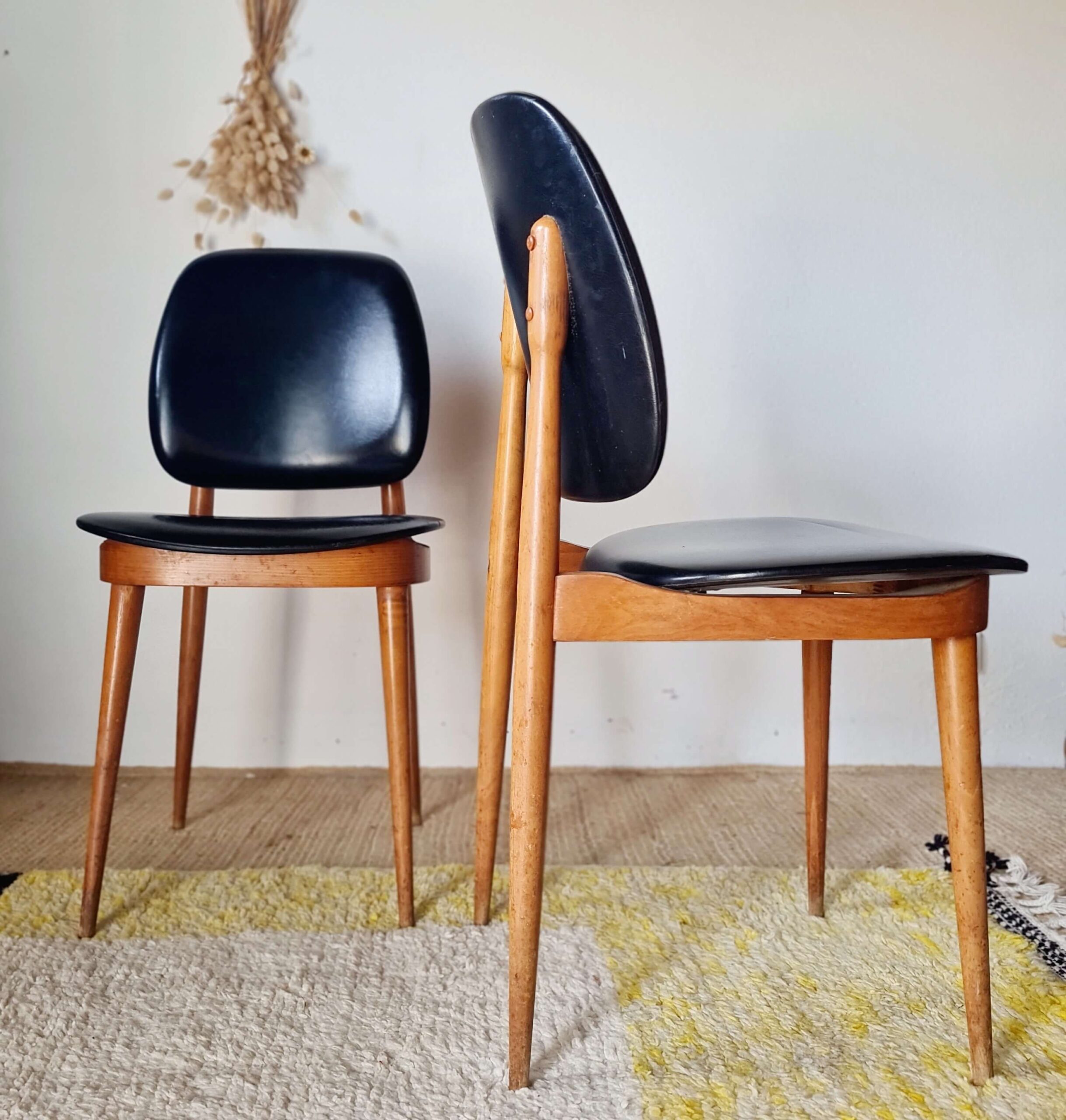 Paire de chaises de salon des années 1960 avec structure en bois clair, pieds compas fuselés et revêtement en vinyle noir.
