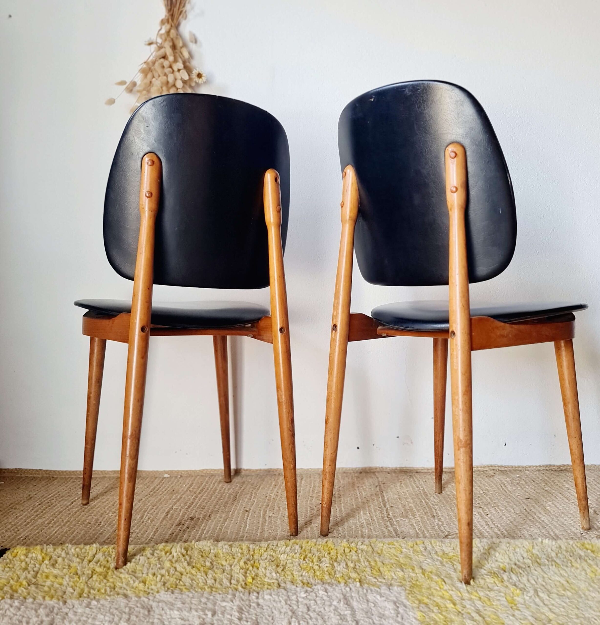 Vue rapprochée de la structure inférieure d'une chaise scandinave des années 60, mettant en valeur l'assemblage en bois clair verni et ledessous de l'assise noire.