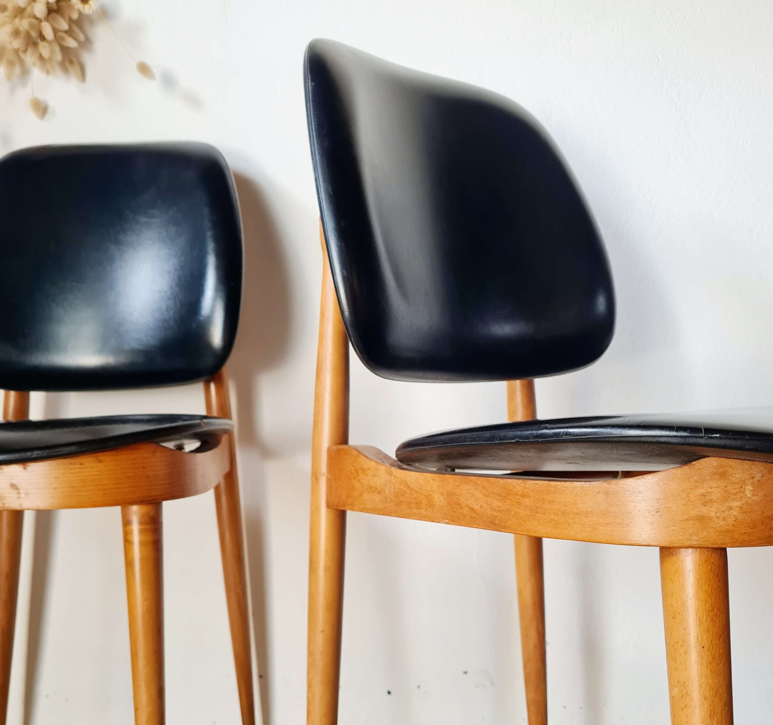 Paire de chaises de style moderniste des années 60, l'une de profil et l'autre de face, avec structure en bois clair et revêtement noir, posées sur un tapis texturé.