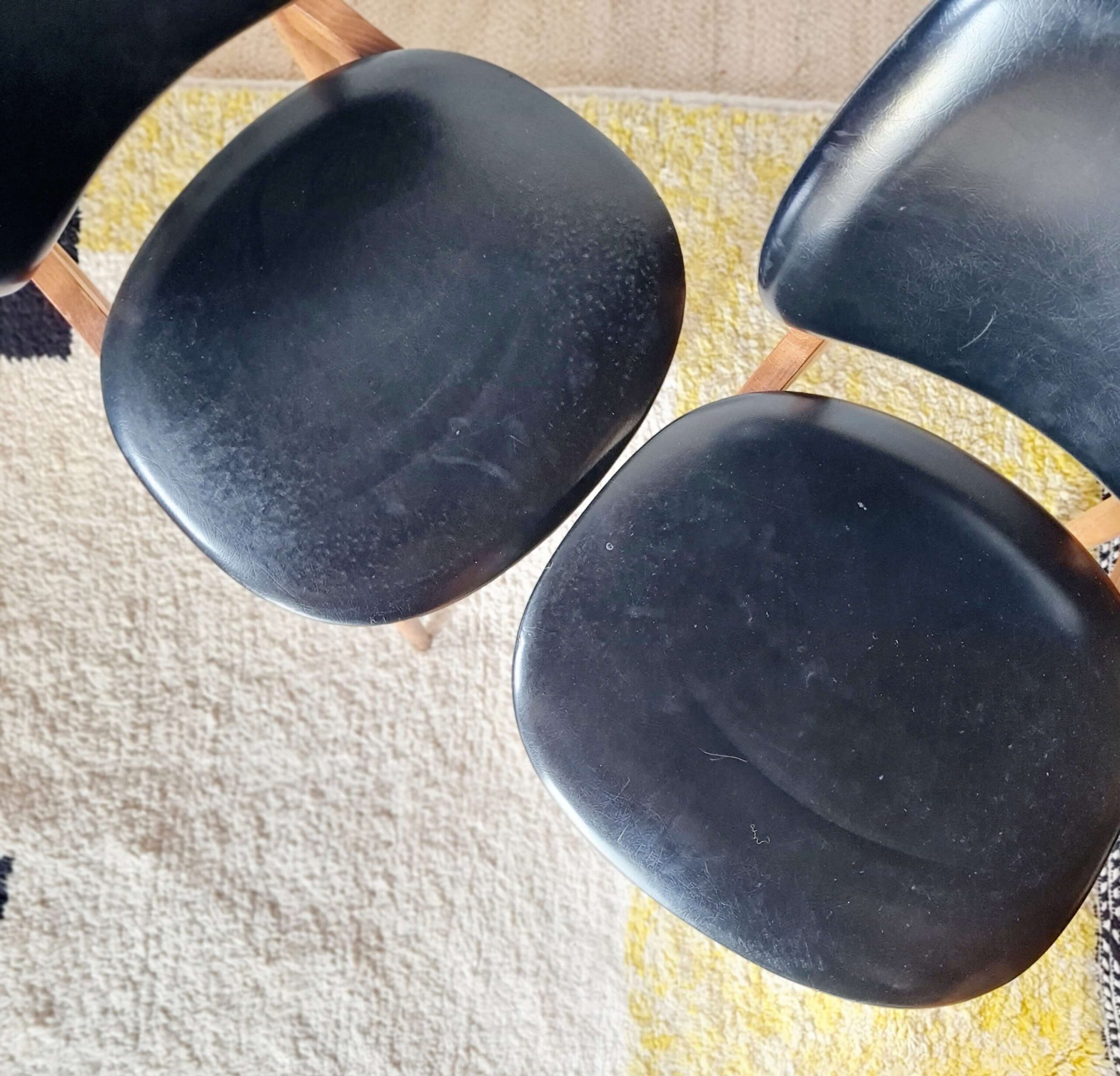Vue du dessus en plongée de deux assises de chaises vintage des années 60 en skaï noir mat.