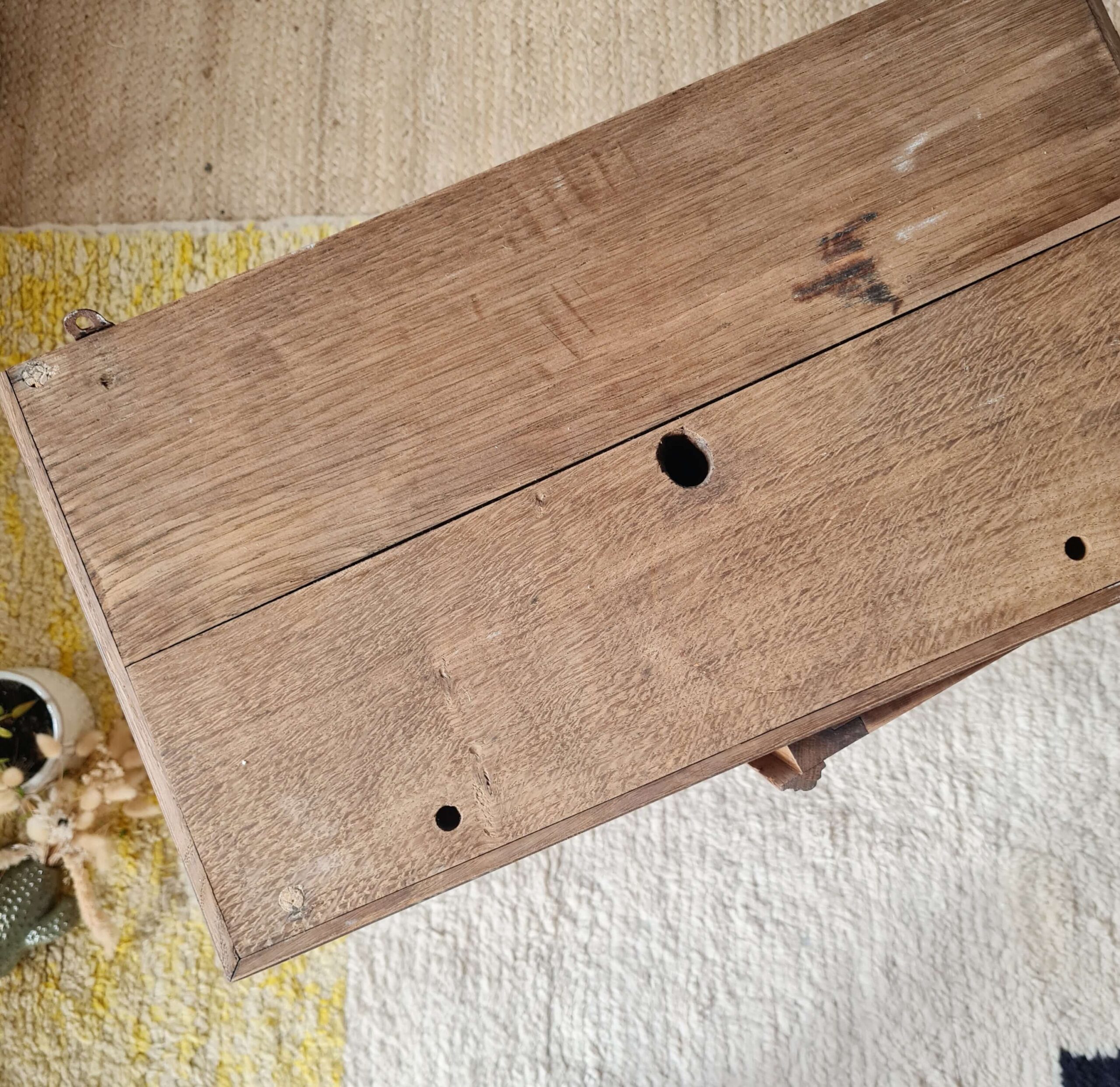 Vue plongeante sur le dessus en bois brut d'une petite armoire ancienne, révélant les veines et l'usure naturelle du temps.