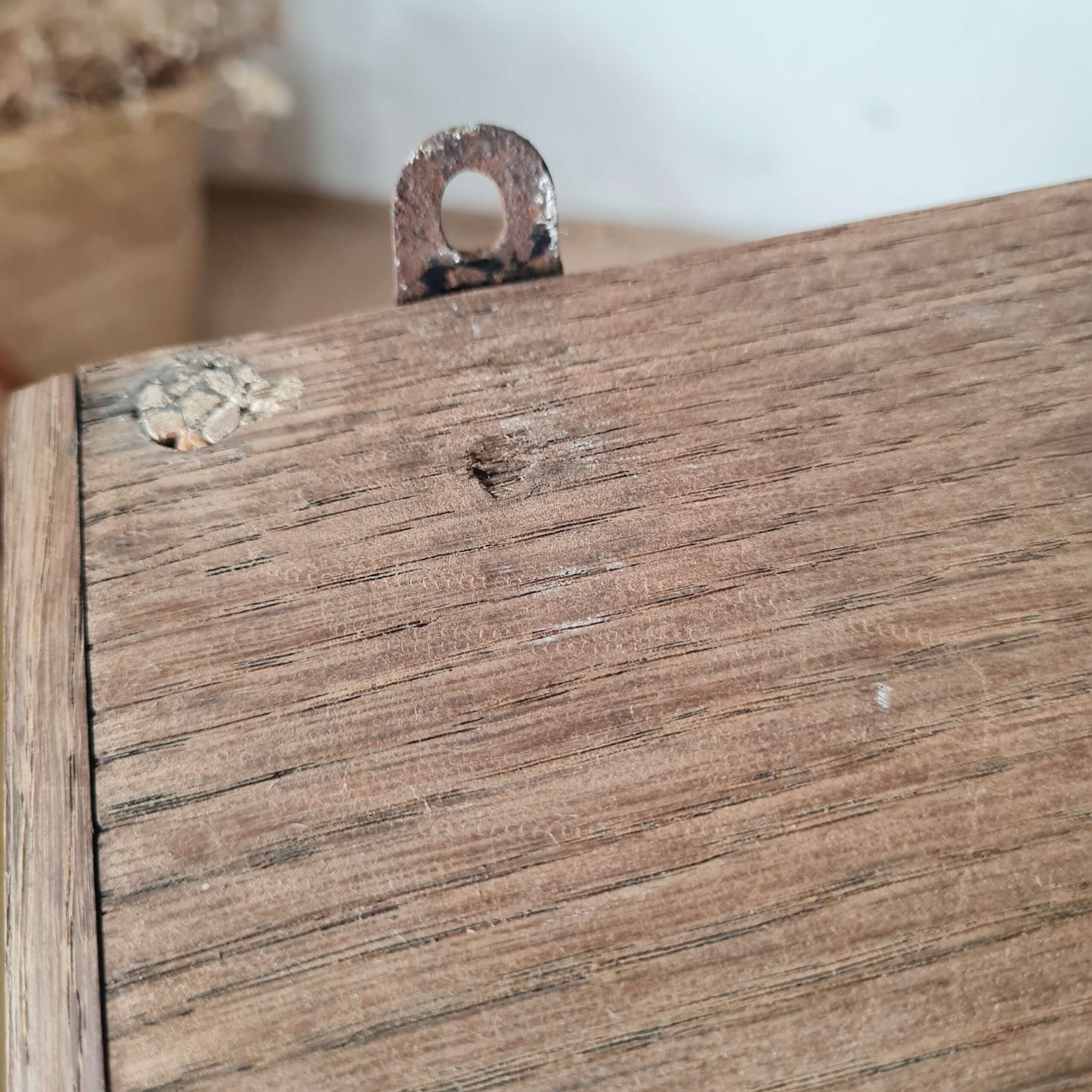 Gros plan sur une patte de fixation murale en métal vieilli d'origine, vissée sur le haut en bois de l'armoire de pharmacie.