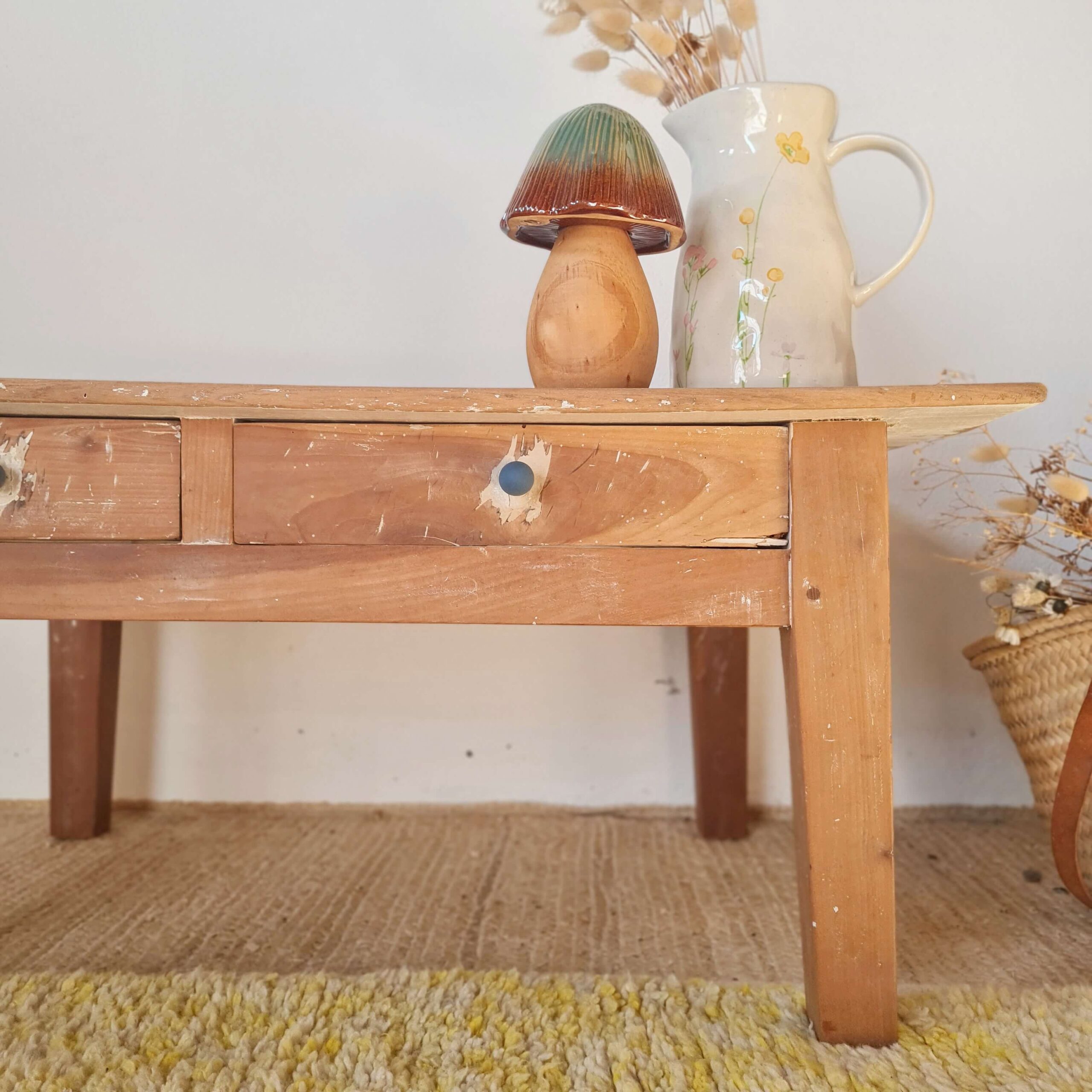Détail du tiroir gauche en bois d'une table basse ancienne avec un petit bouton bleu et des traces de peinture blanche