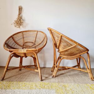 Deux fauteuils coquille en rotin tressé disposés côte à côte, décorés de fleurs séchées suspendues au mur.