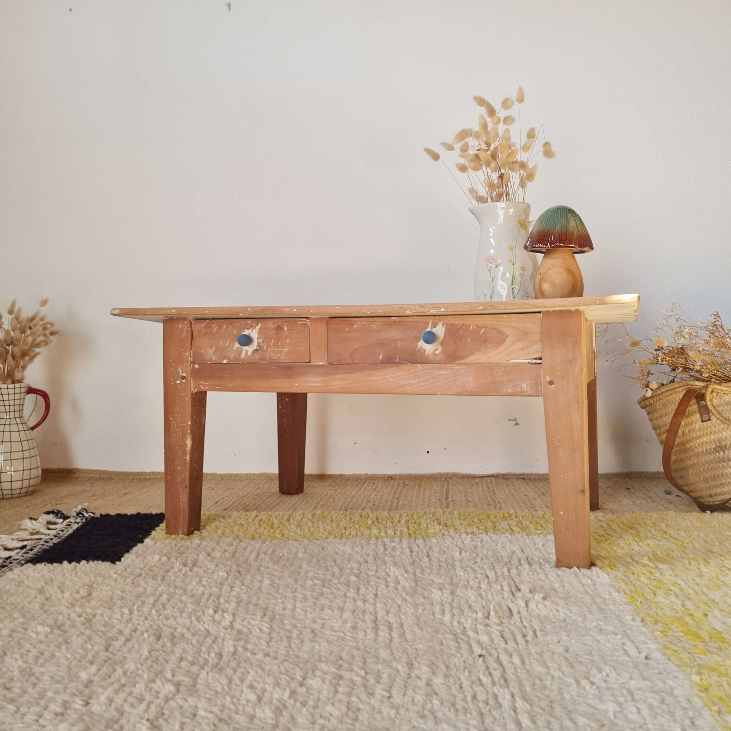Table basse de ferme vintage en bois brut à deux tiroirs installée dans un salon sur un tapis de style berbère