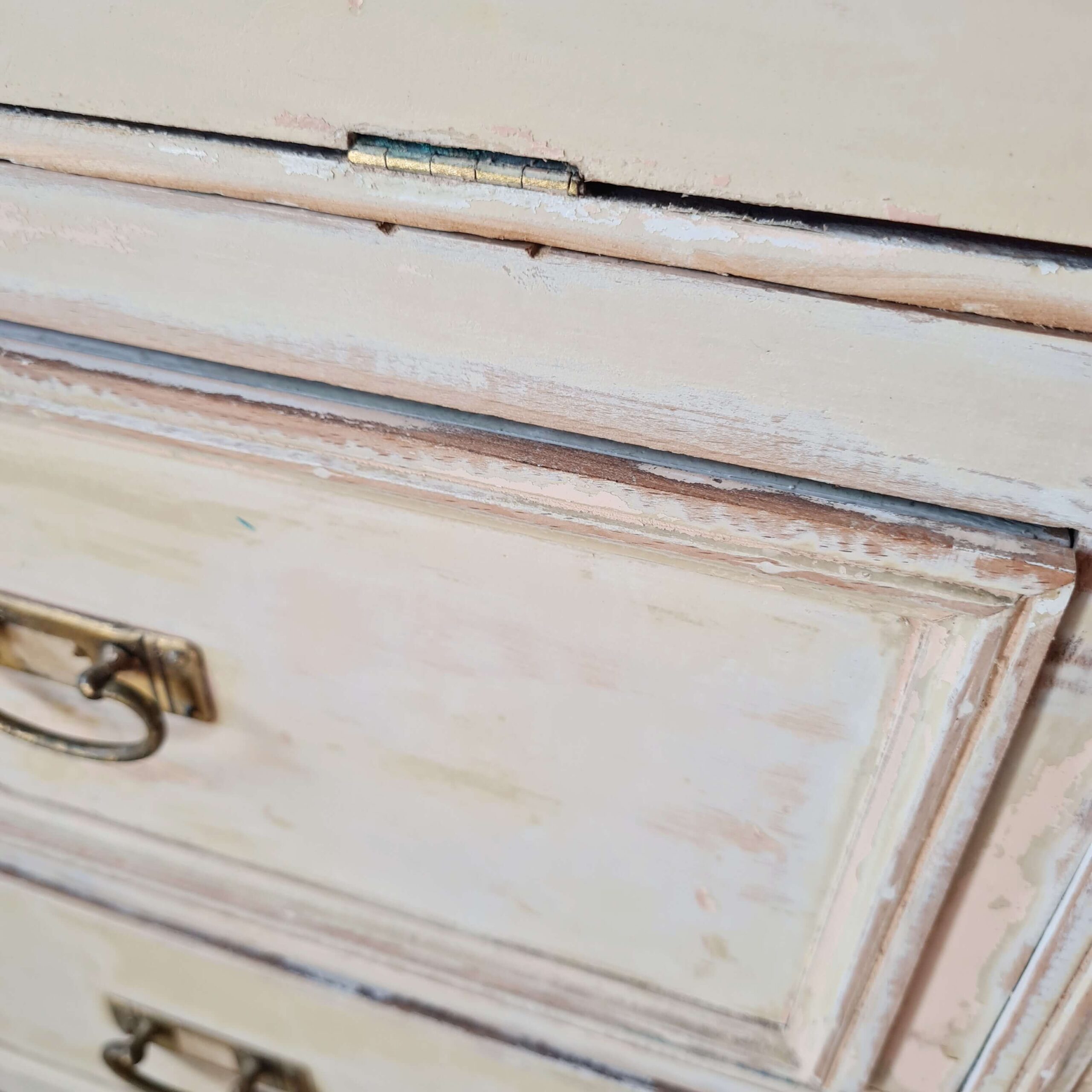 Détail technique d'une charnière métallique sur le tiroir d'un meuble de métier ancien, témoignant de sa restauration ou de son authenticité.