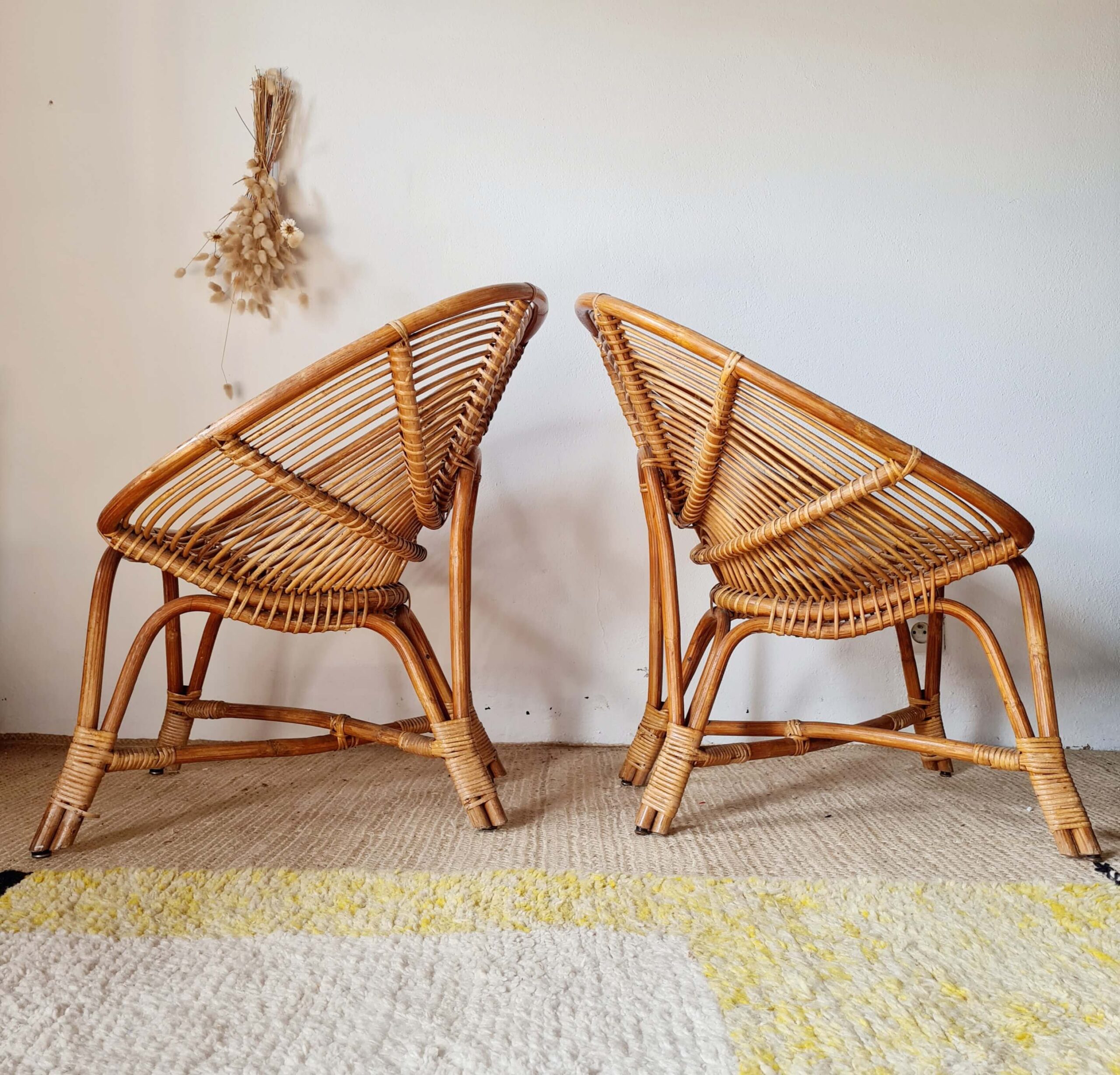 Vue de côté d'une paire de fauteuils anciens en rotin tressé, mettant en valeur la forme arrondie et la structure artisanale