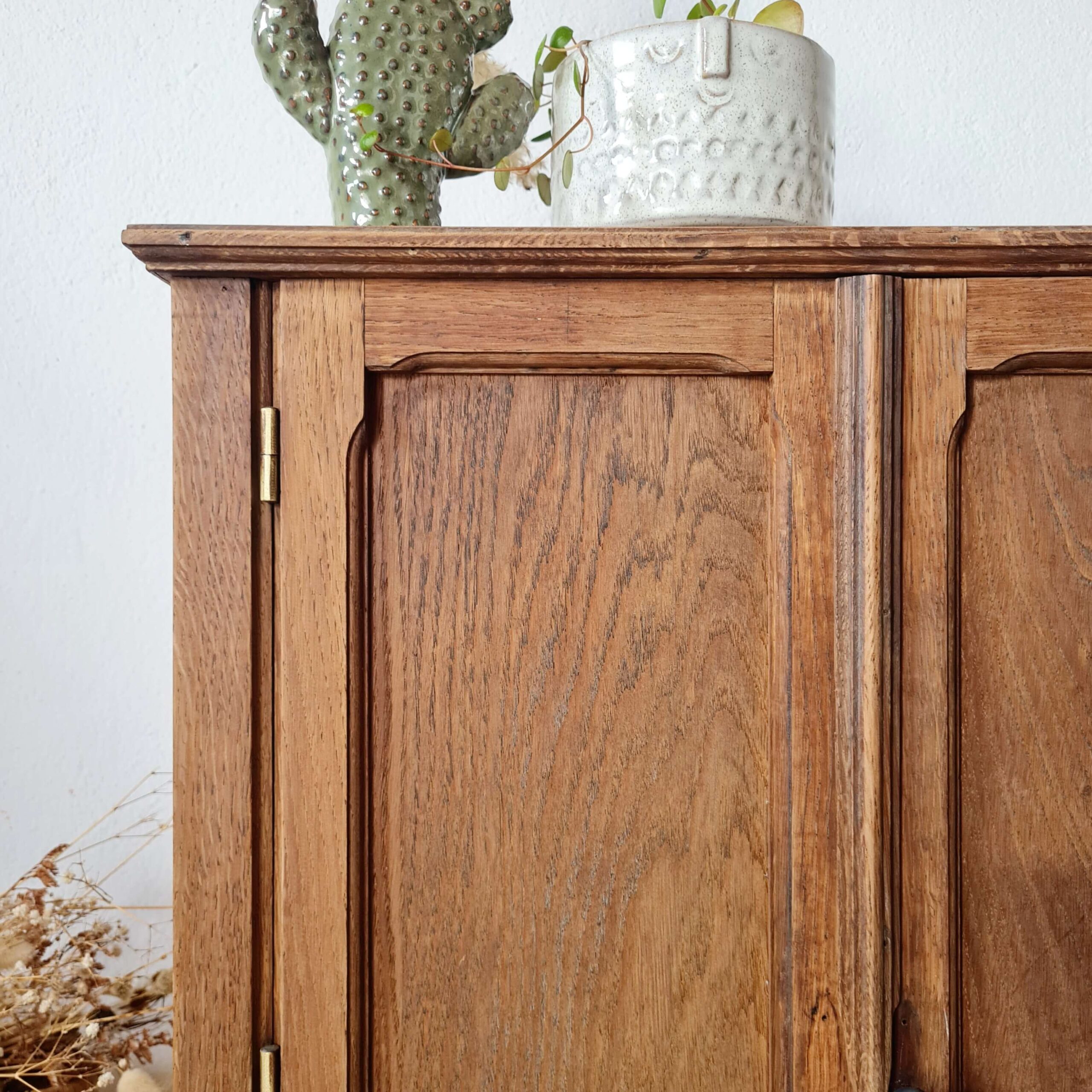 Détail de la corniche en bois massif d'une petite armoire ancienne, décorée avec un cactus en céramique.