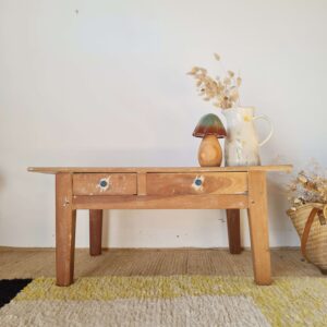 Table basse de ferme vintage en bois brut avec deux tiroirs de face, décorée d'un vase en céramique et d'un champignon en bois