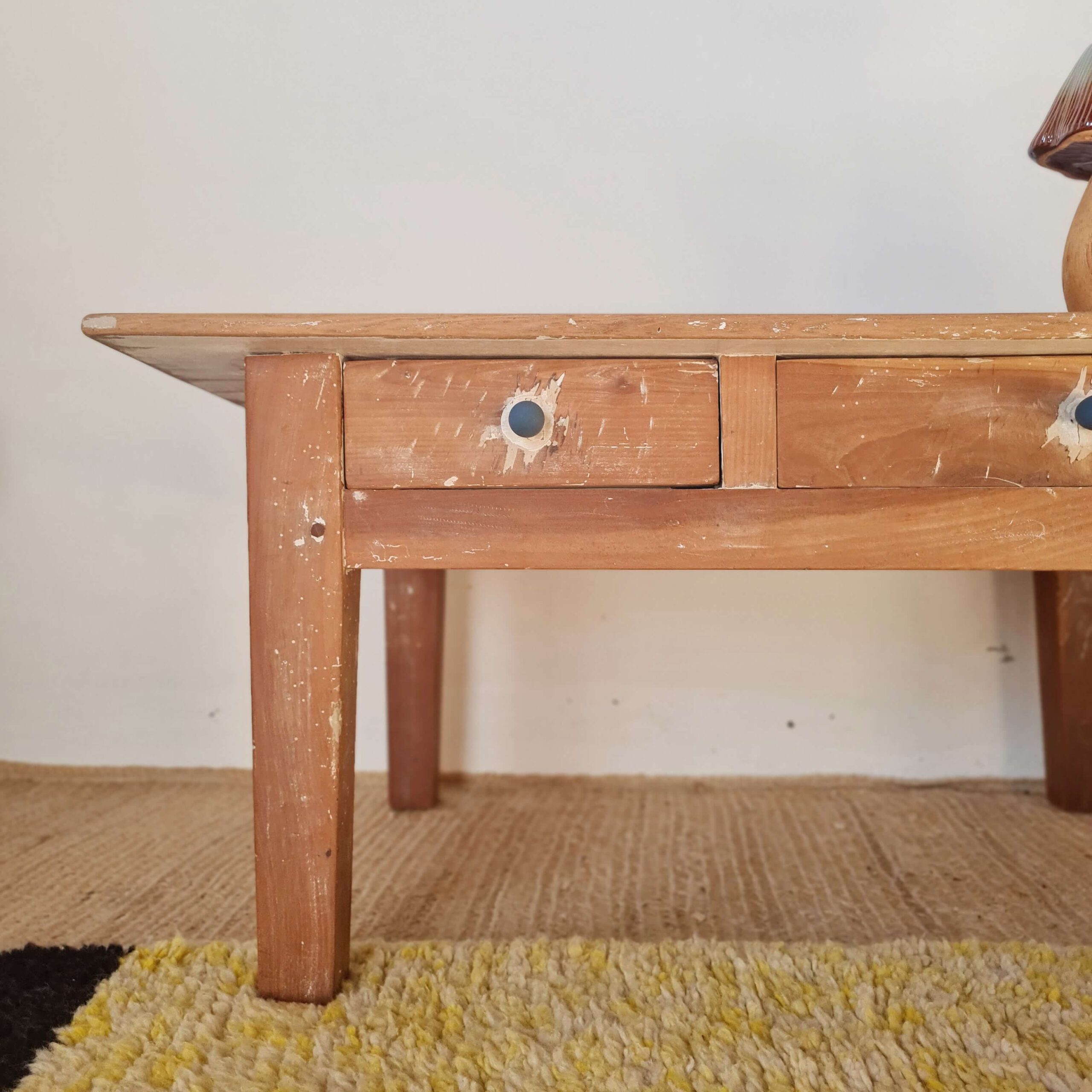 Gros plan sur un tiroir en bois brut avec bouton bleu, surmonté d'un champignon en céramique et d'un pichet vintage