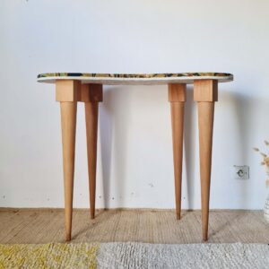 Vue de face d'une table haricot vintage des années 50 en bois clair avec quatre pieds compas fuselés, posée sur un tapis texturé