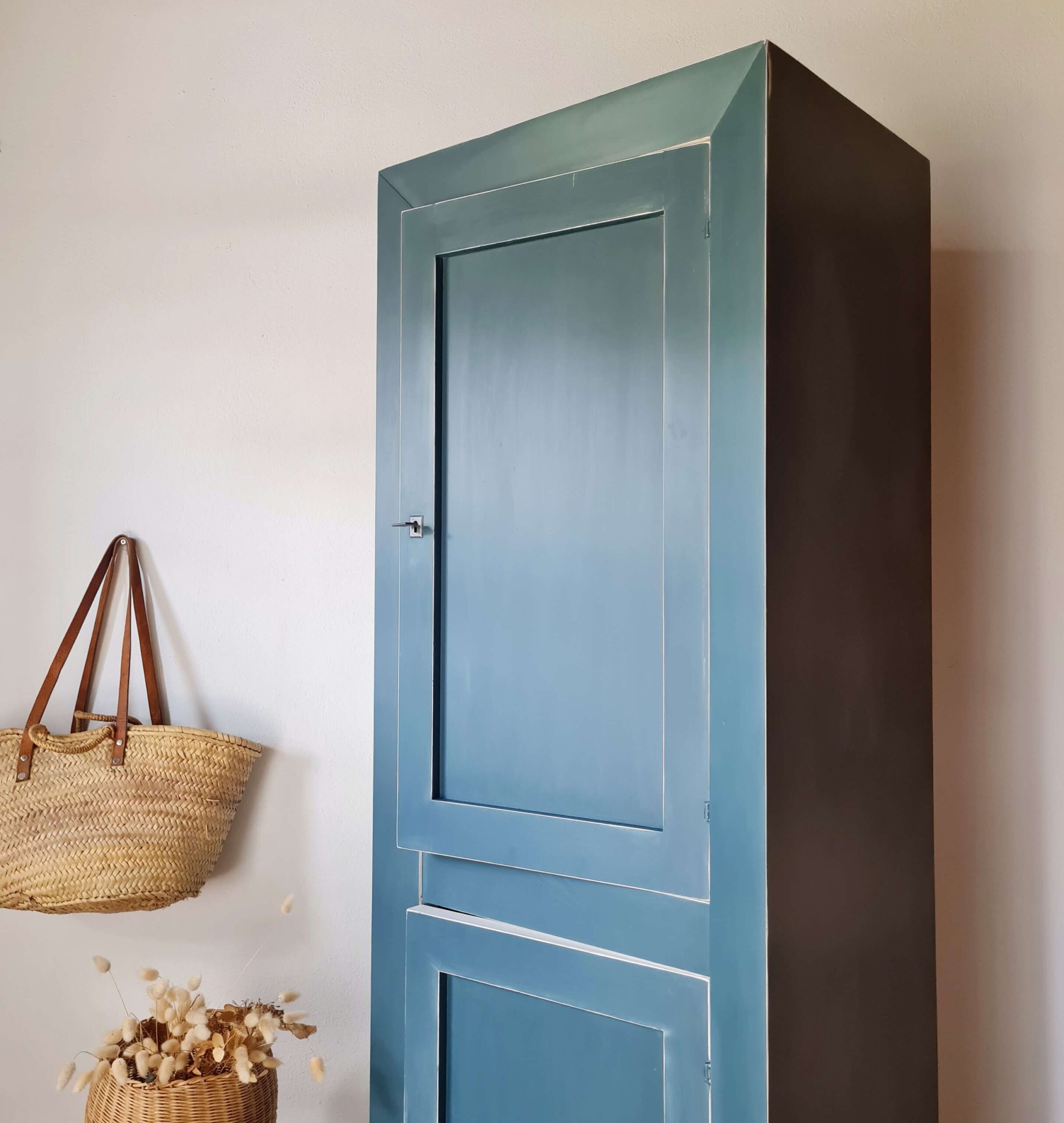Vue d'ensemble en perspective d'une armoire haute bleue de style rustique, décorée avec un panier en osier