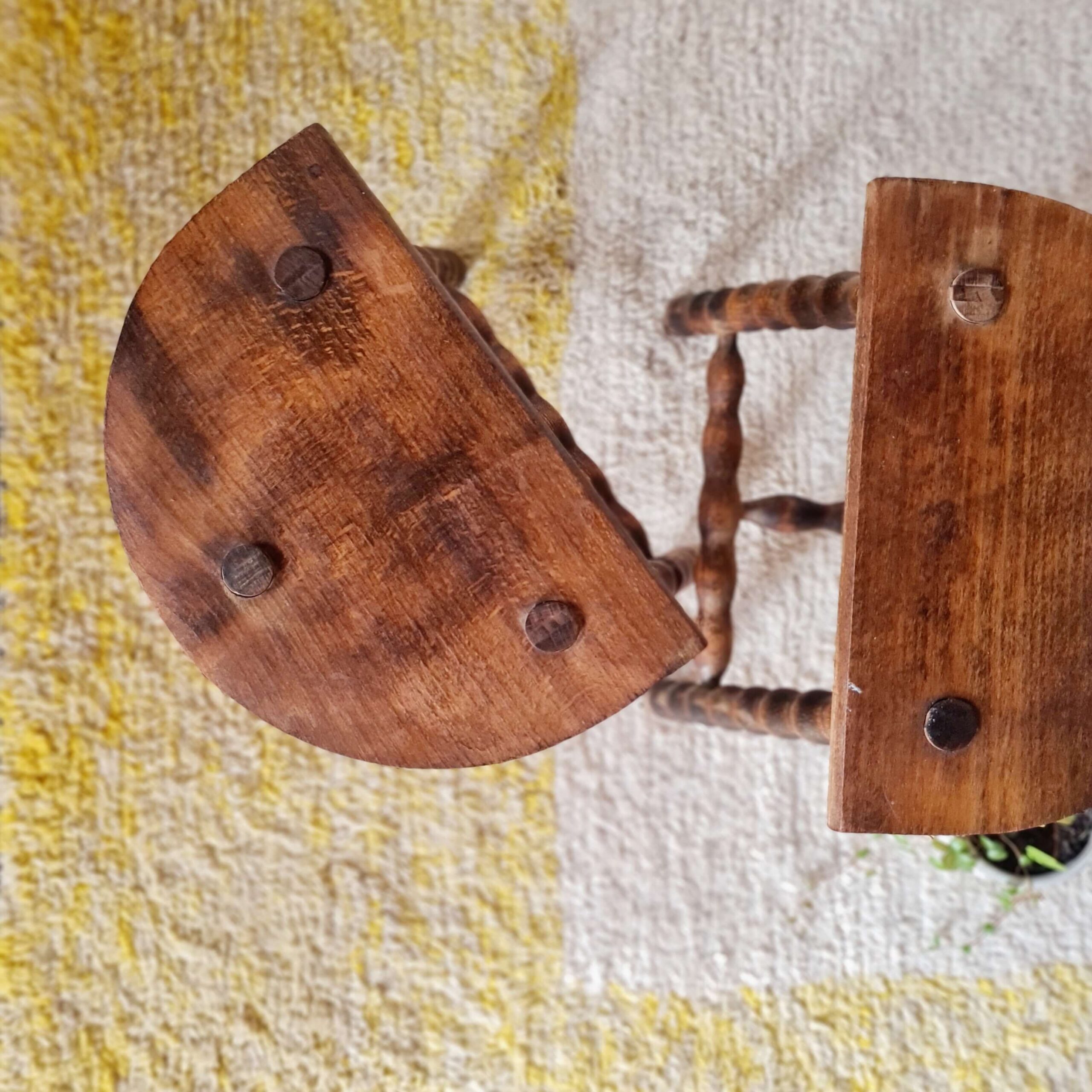 Vue plongeante sur une paire de tabourets en bois massif, révélant la forme en demi-lune de leurs assises et les trois fixations à tenons apparentes.