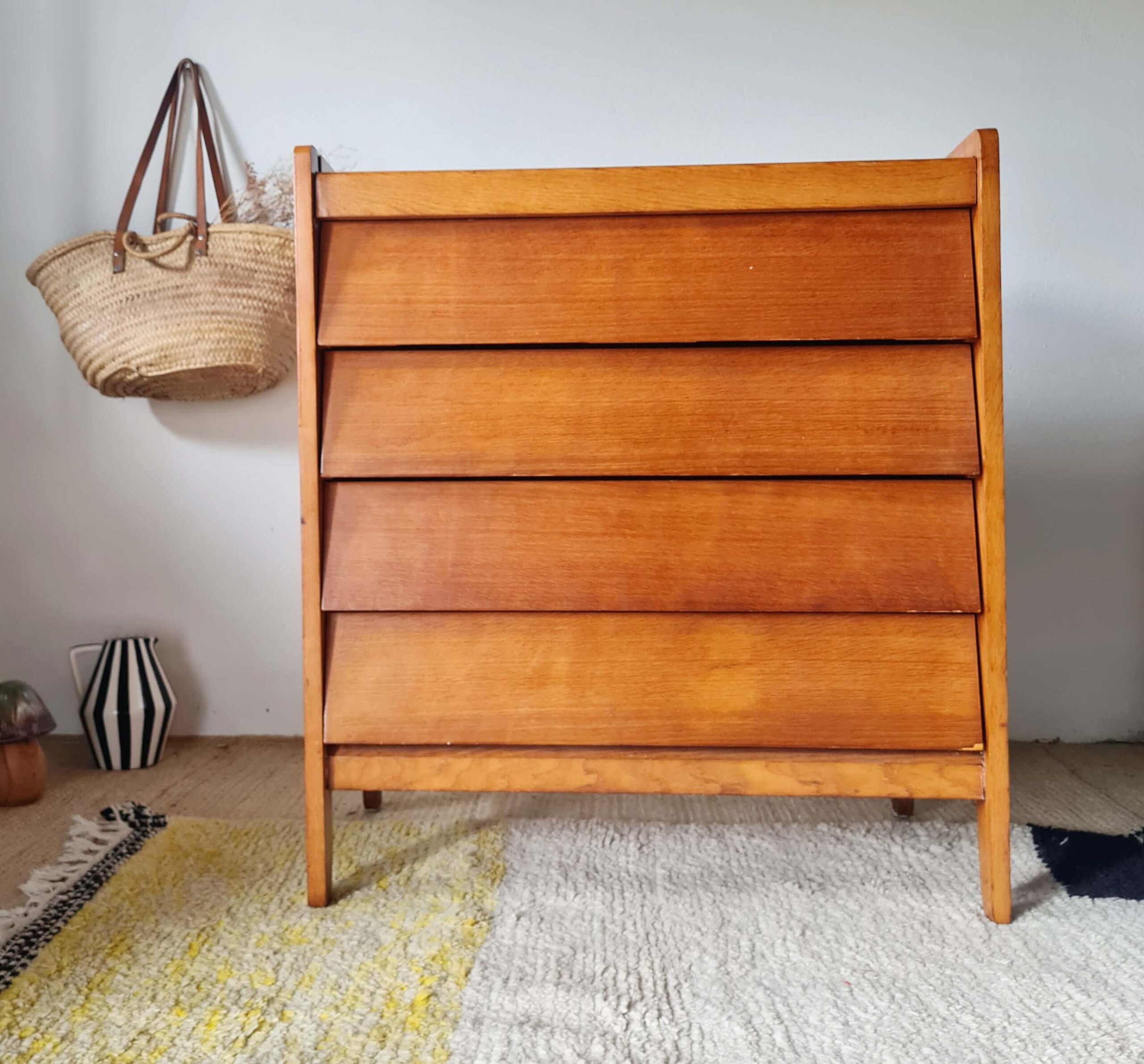 Commode en chêne doré mid-century à 4 tiroirs inclinés présentée de face dans un intérieur à la décoration bohème.