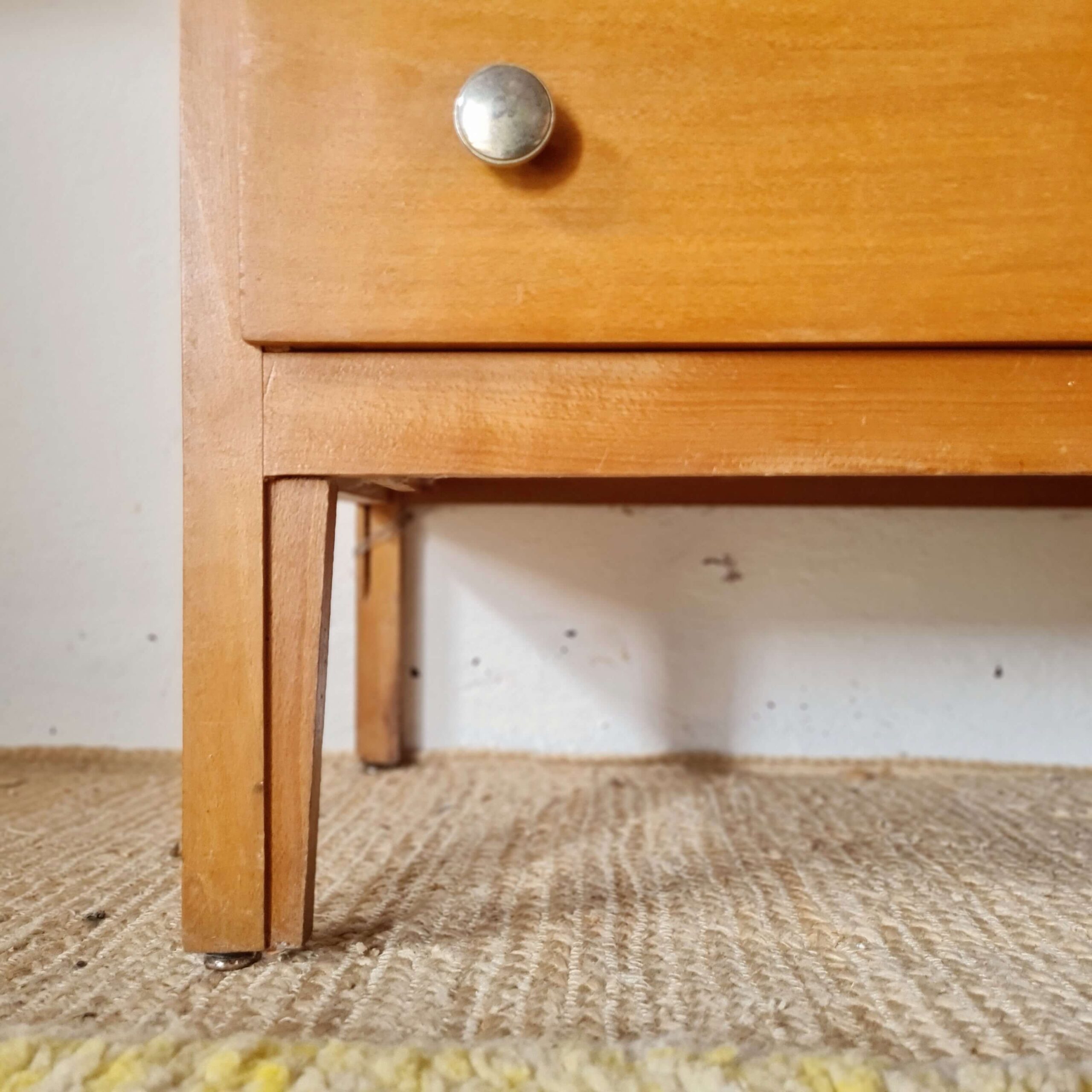 Zoom sur les pieds obliques en bois et le bas d'une commode scandinave des années 60.