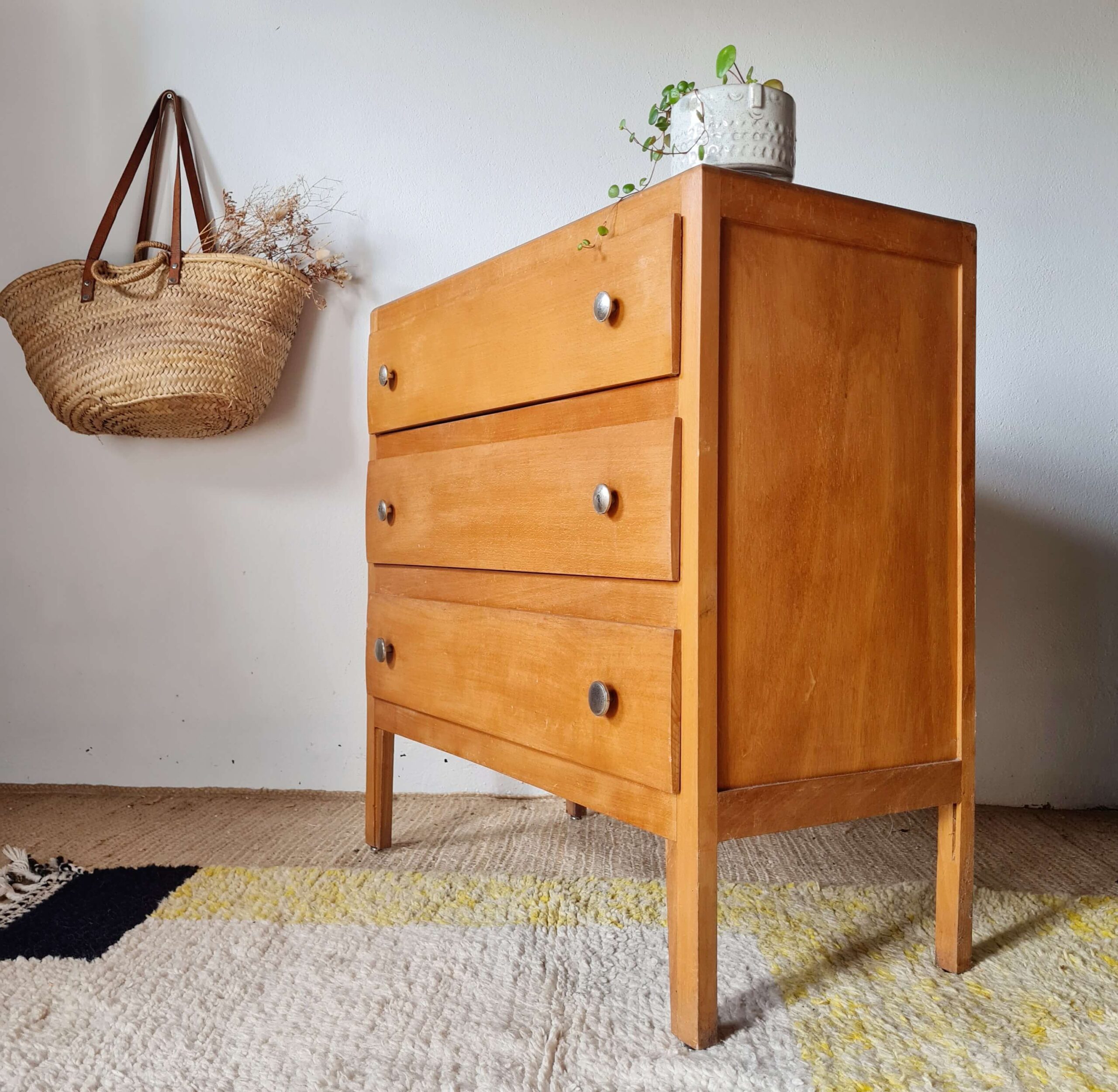 Vue de trois-quarts profil d'une commode vintage en bois style scandinave sur un tapis beige.