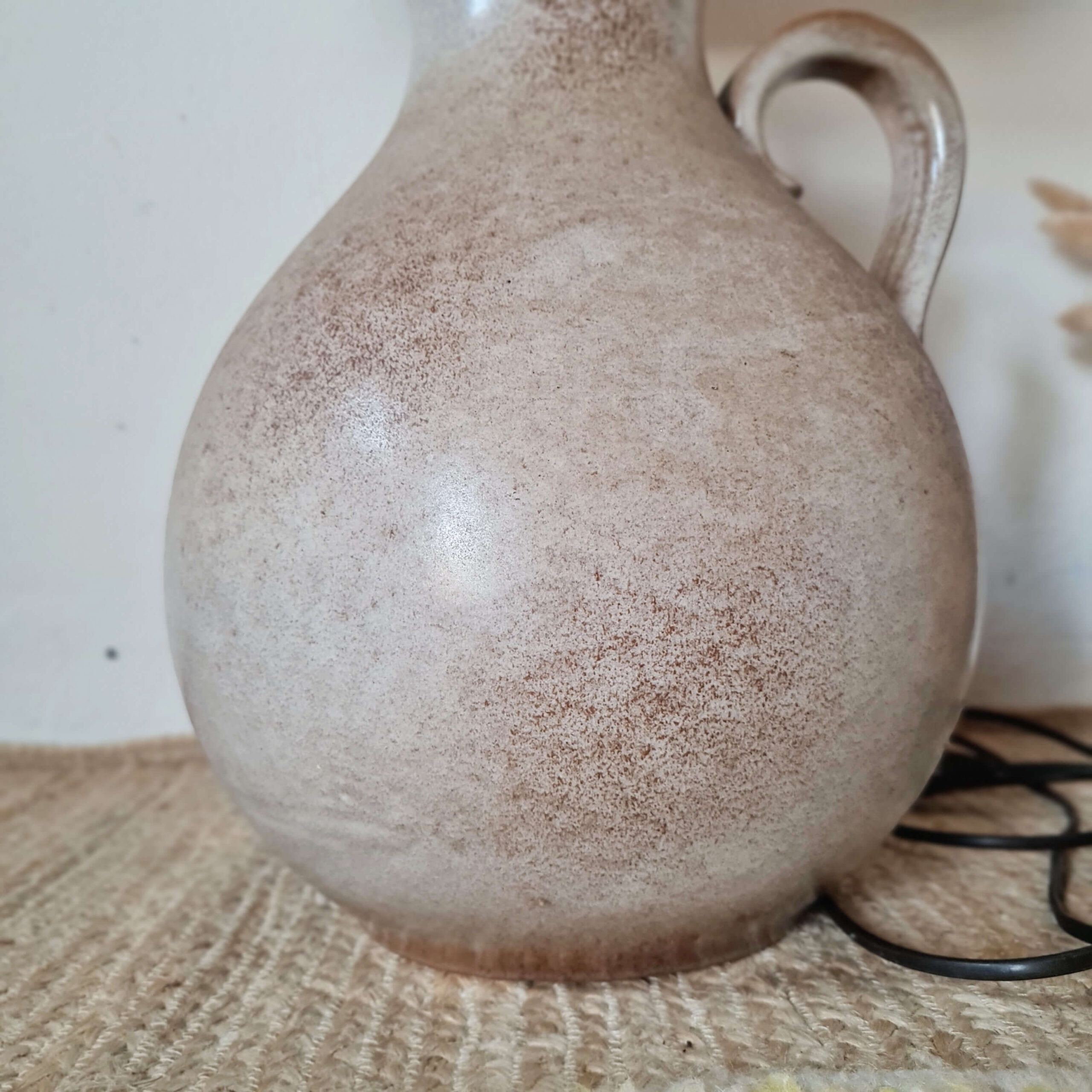 Détail de la glaçure artisanale mouchetée d'une lampe en céramique beige.