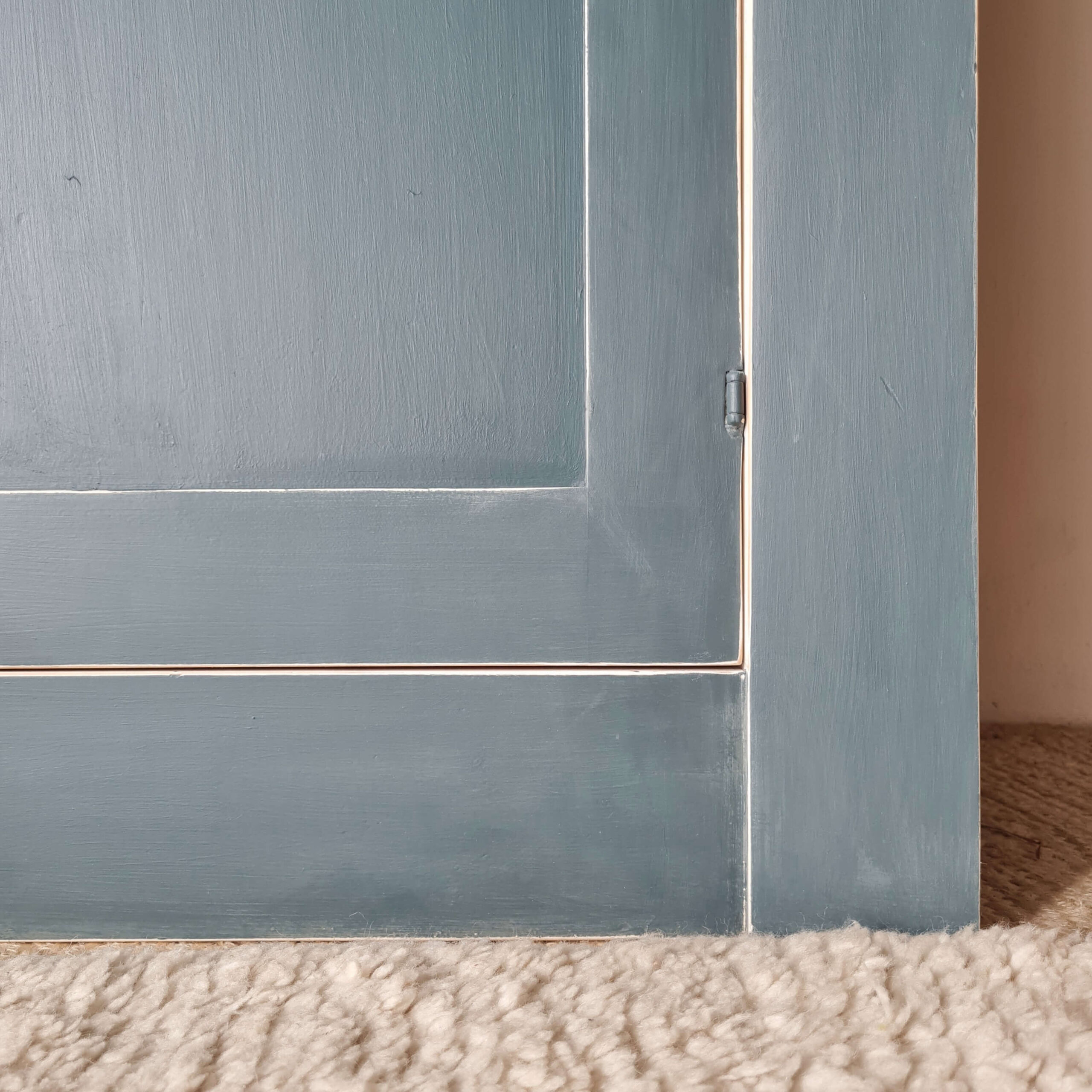 Gros plan sur la charnière métallique d'une porte d'armoire bleue, mettant en valeur son style vintage.