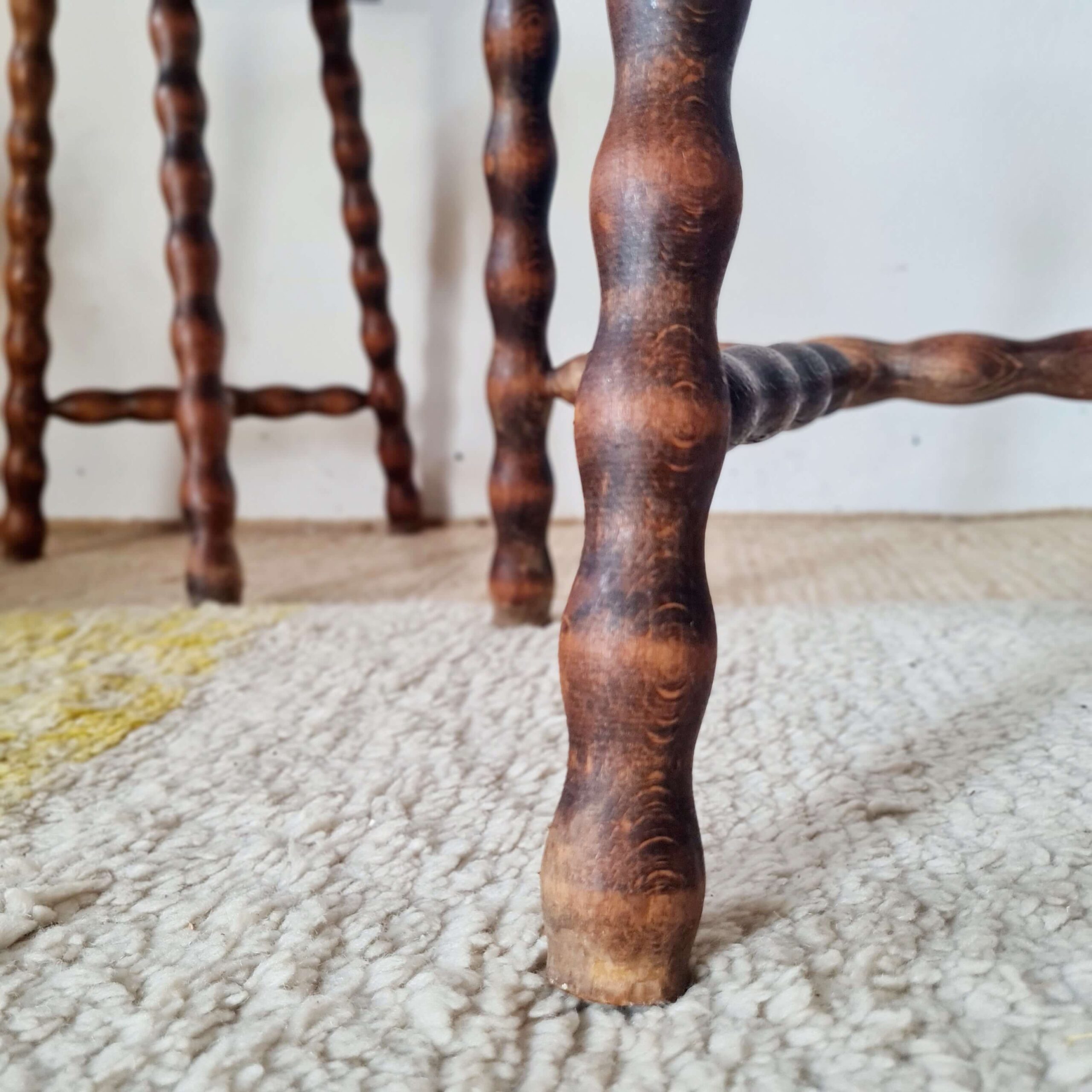 Détail du pied tourné d'un tabouret ancien, illustrant la qualité du travail artisanal du bois