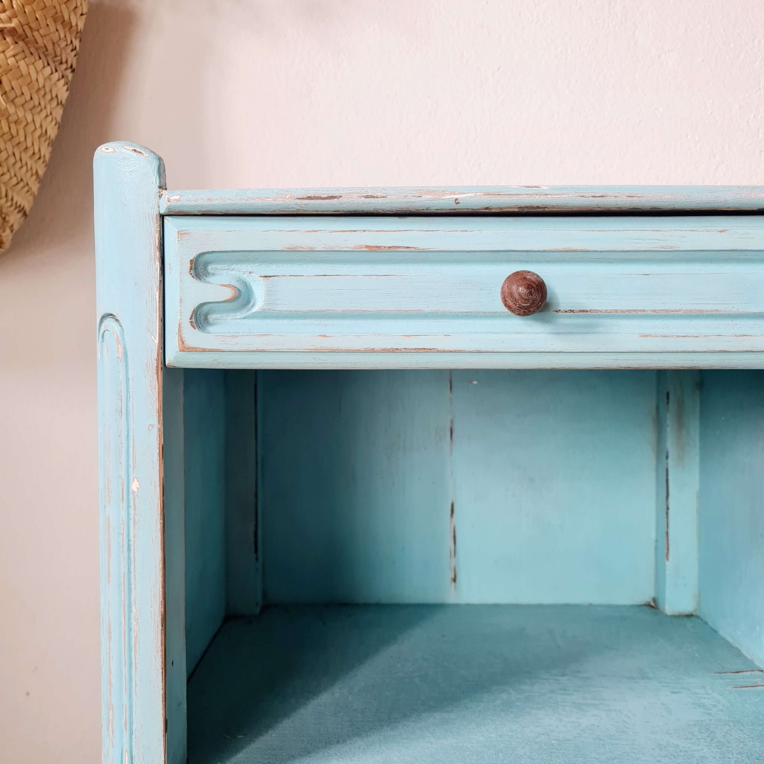 Gros plan sur le tiroir sculpté et le bouton en bois d'un petit meuble d'appoint bleu turquoise ancien