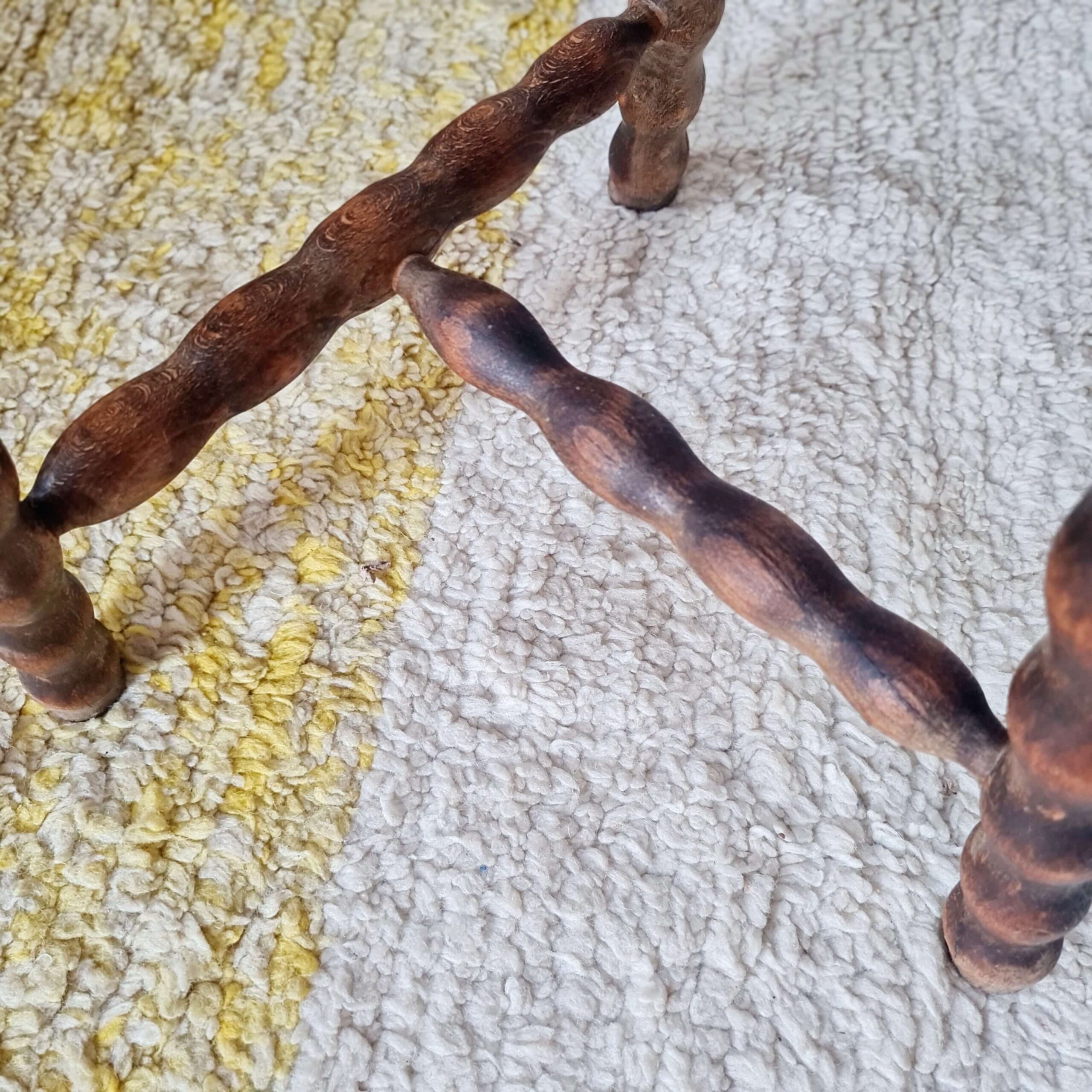 Gros plan sur l'entretoise d'un tabouret tripode en bois tourné aux pieds torsadés
