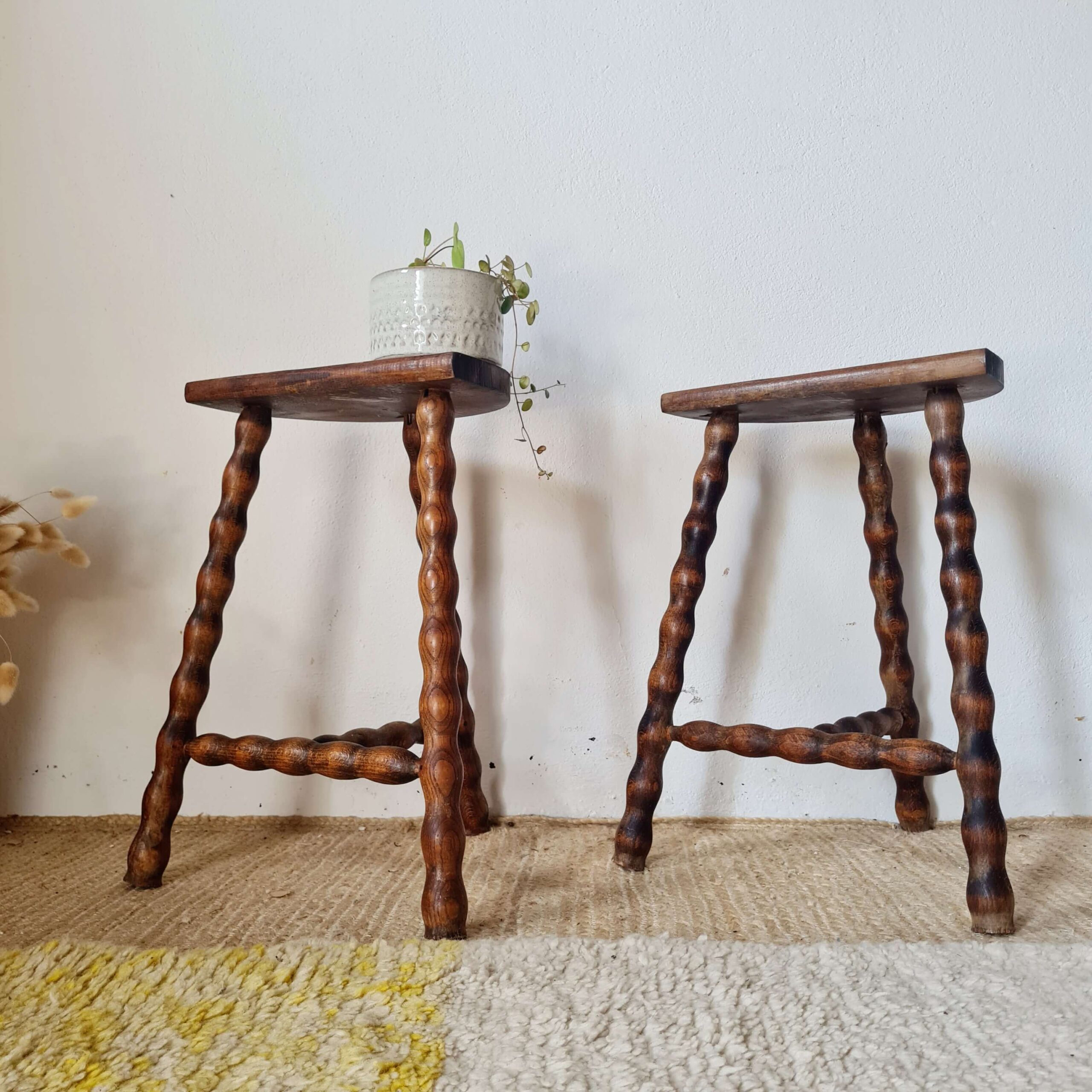 Paire de tabourets tripodes vintage en bois tourné torsadé présentés dans une décoration d'intérieur bohème