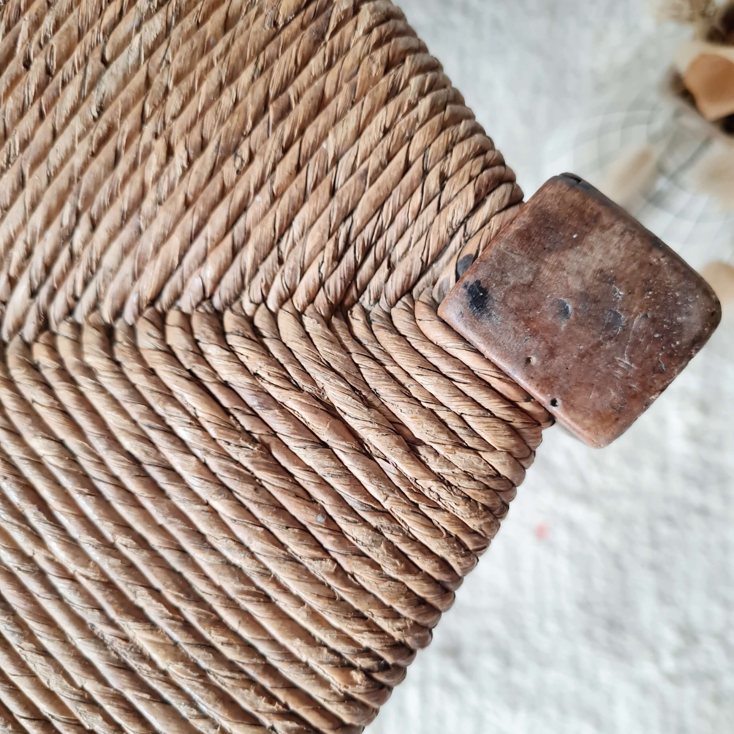 Gros plan sur l'angle supérieur en bois massif patiné d'un tabouret ancien avec le départ du paillage.