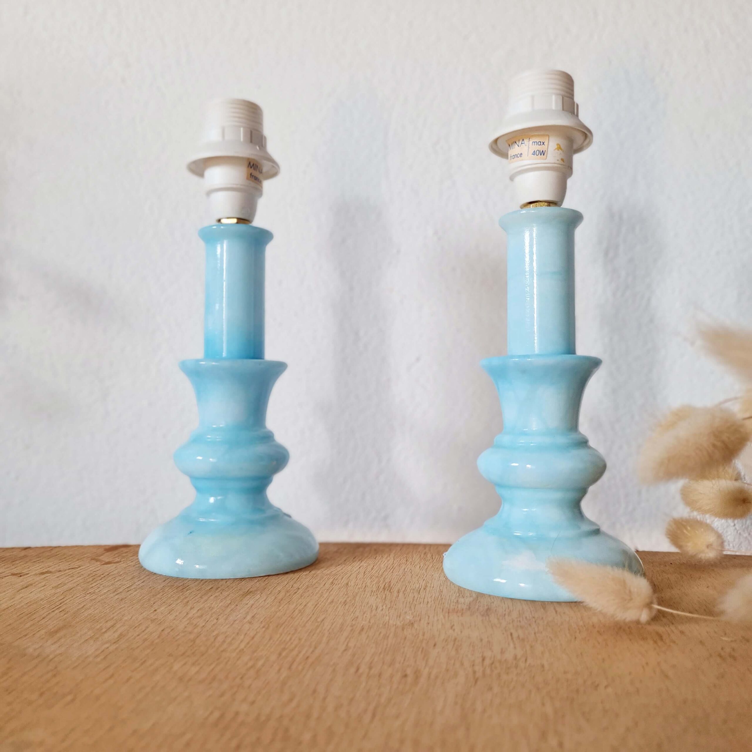 Paire de pieds de lampe vintage en opaline bleue posée sur un meuble en bois à côté de fleurs séchées