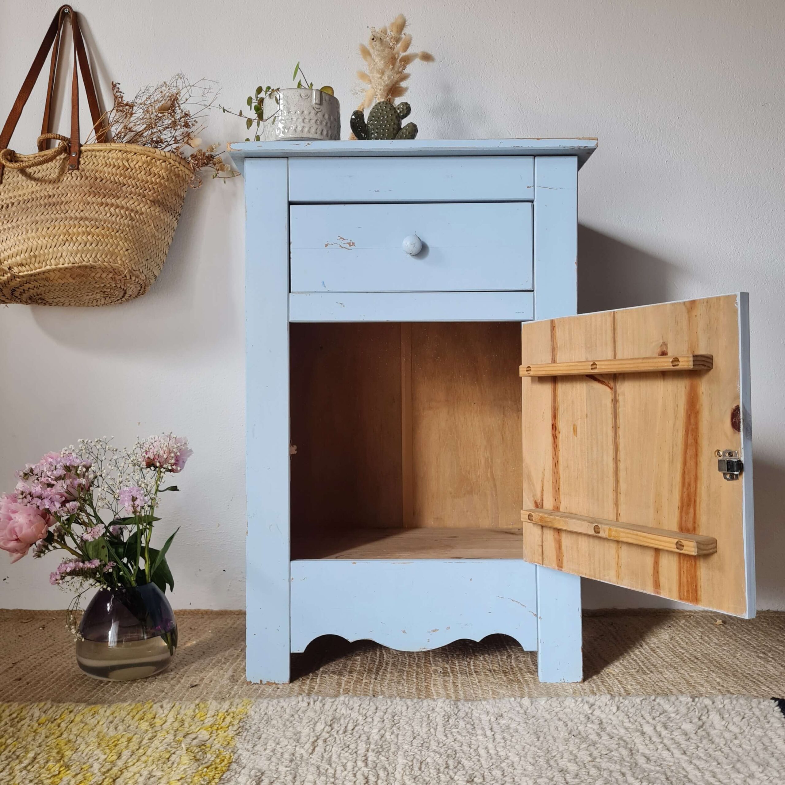 Chiffonnier bleu pastel avec la porte ouverte dévoilant un grand espace de rangement en bois brut.