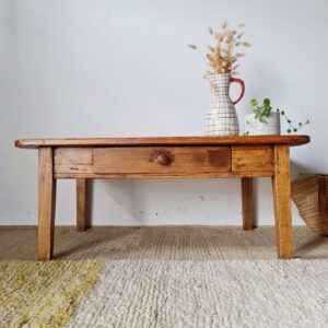 Table de ferme basse ancienne en bois brut avec un grand tiroir central, présentée par Factory Vintage dans une ambiance bohème.
