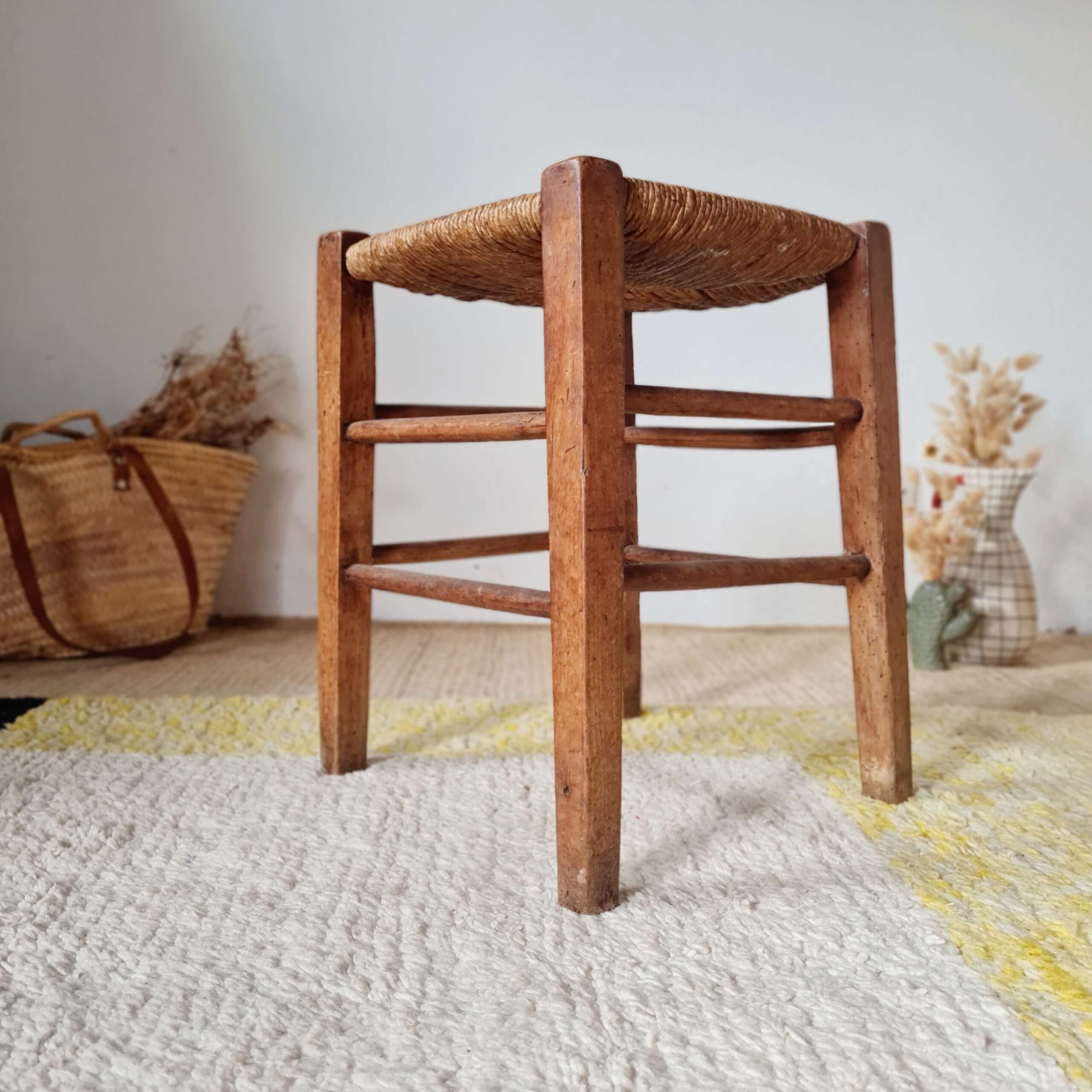Tabouret vintage en bois massif et paille tressée posé sur un tapis, vue de trois quarts.