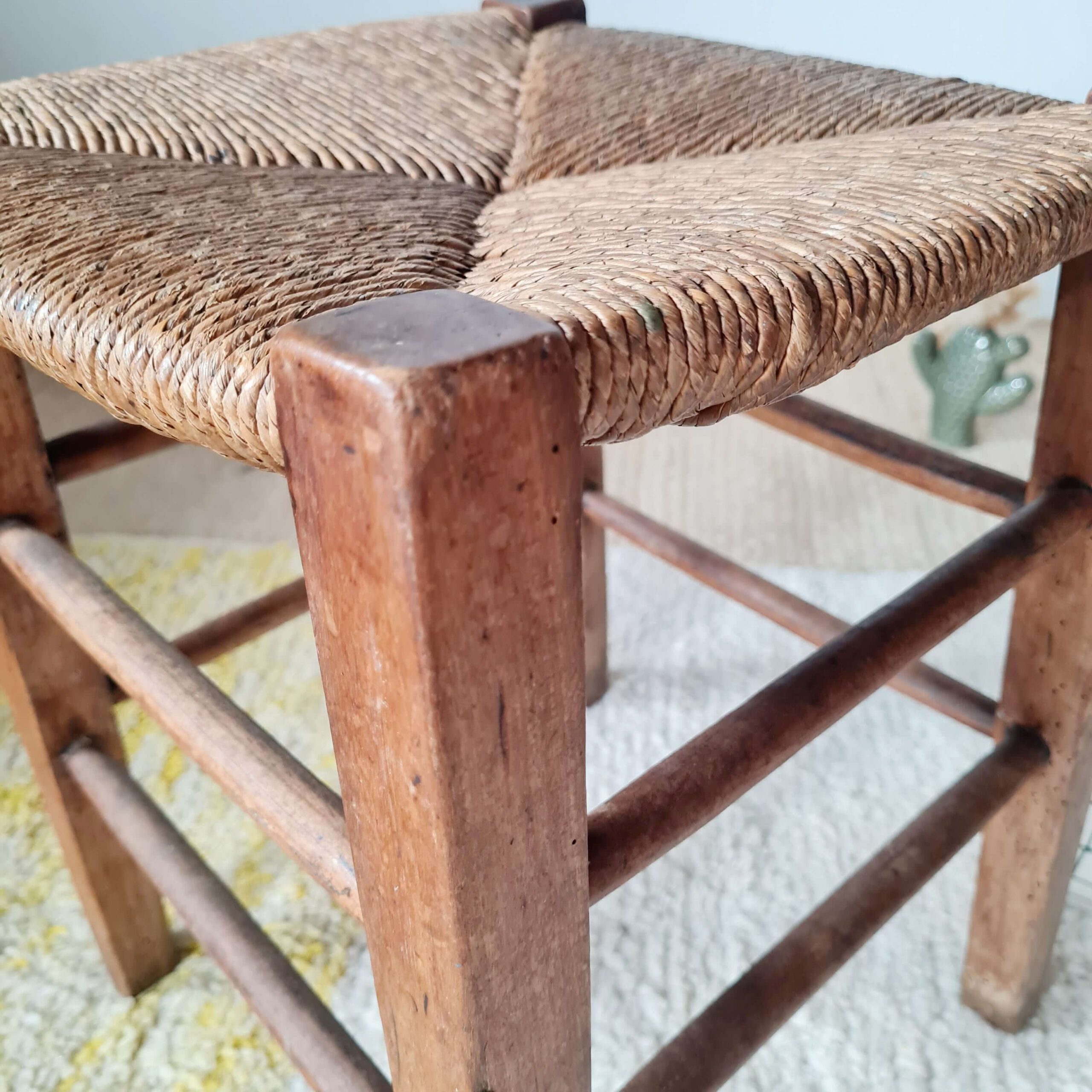 Tabouret ancien de style rustique en bois foncé avec assise paillée et double rangée de barreaux repose-pieds.