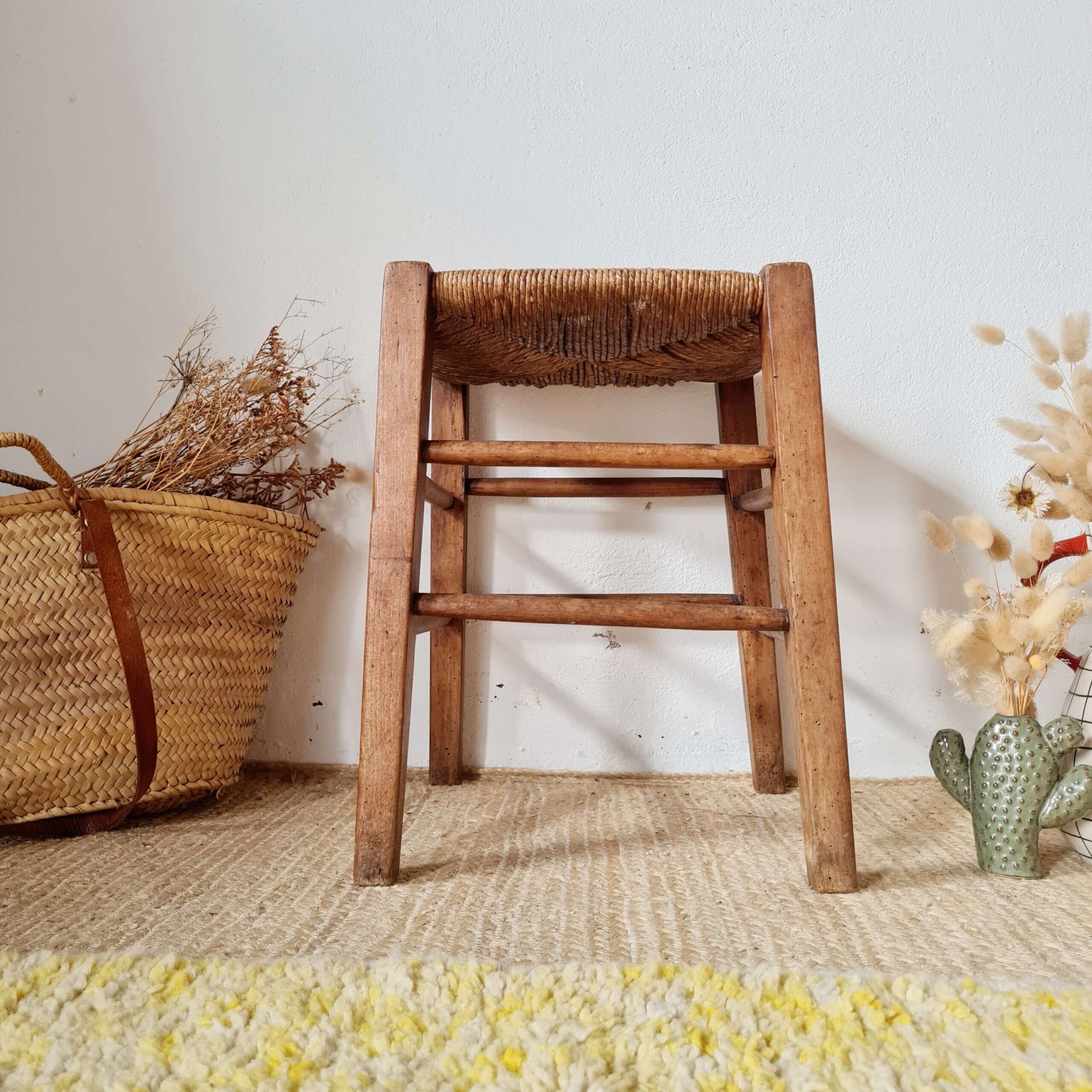Vue de face d'un tabouret ancien en bois patiné avec une assise en paille naturelle.