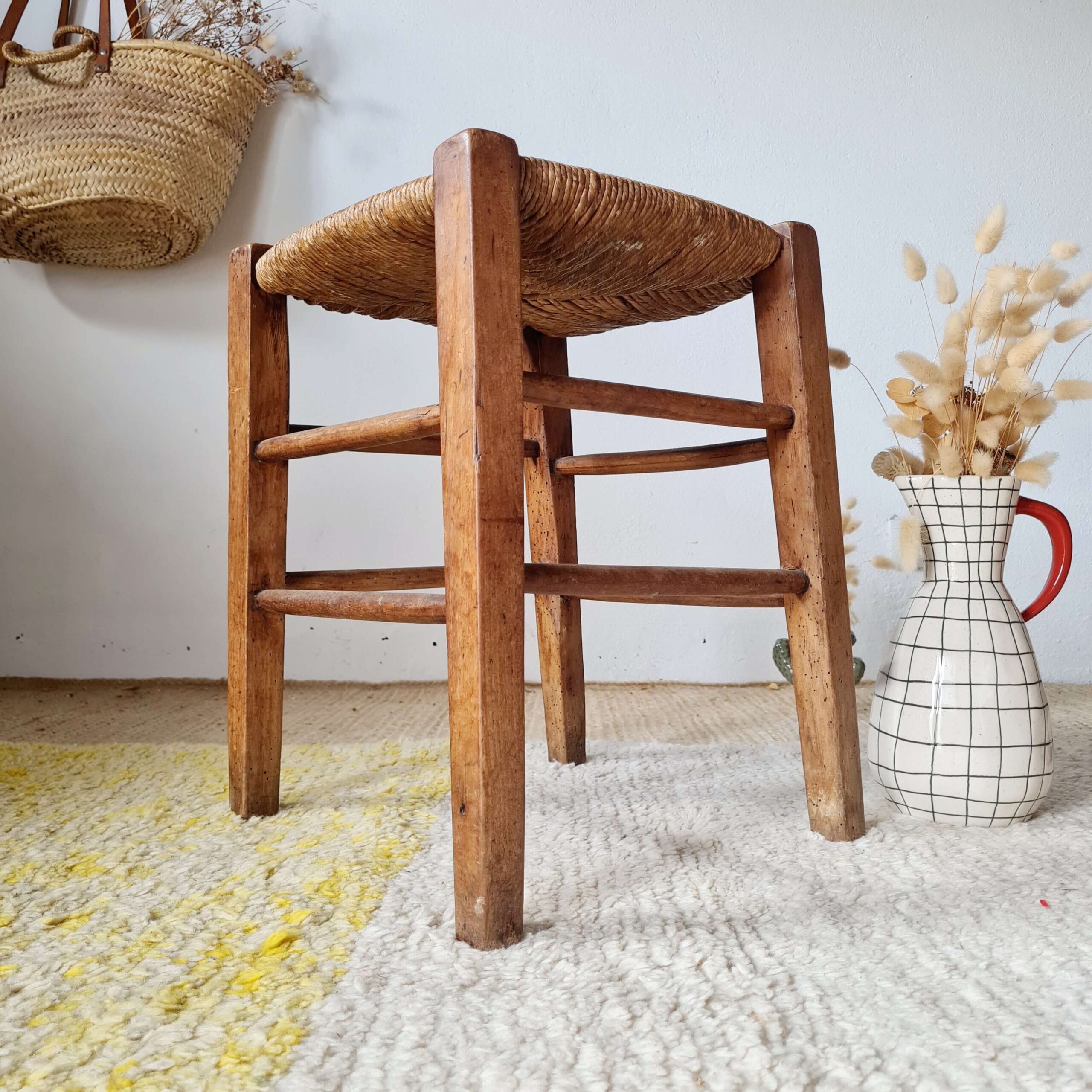 Vue de trois-quarts d'un tabouret rustique en bois massif avec une assise fraîchement repaillée, illustrant le savoir-faire du mobilier de ferme ancien.