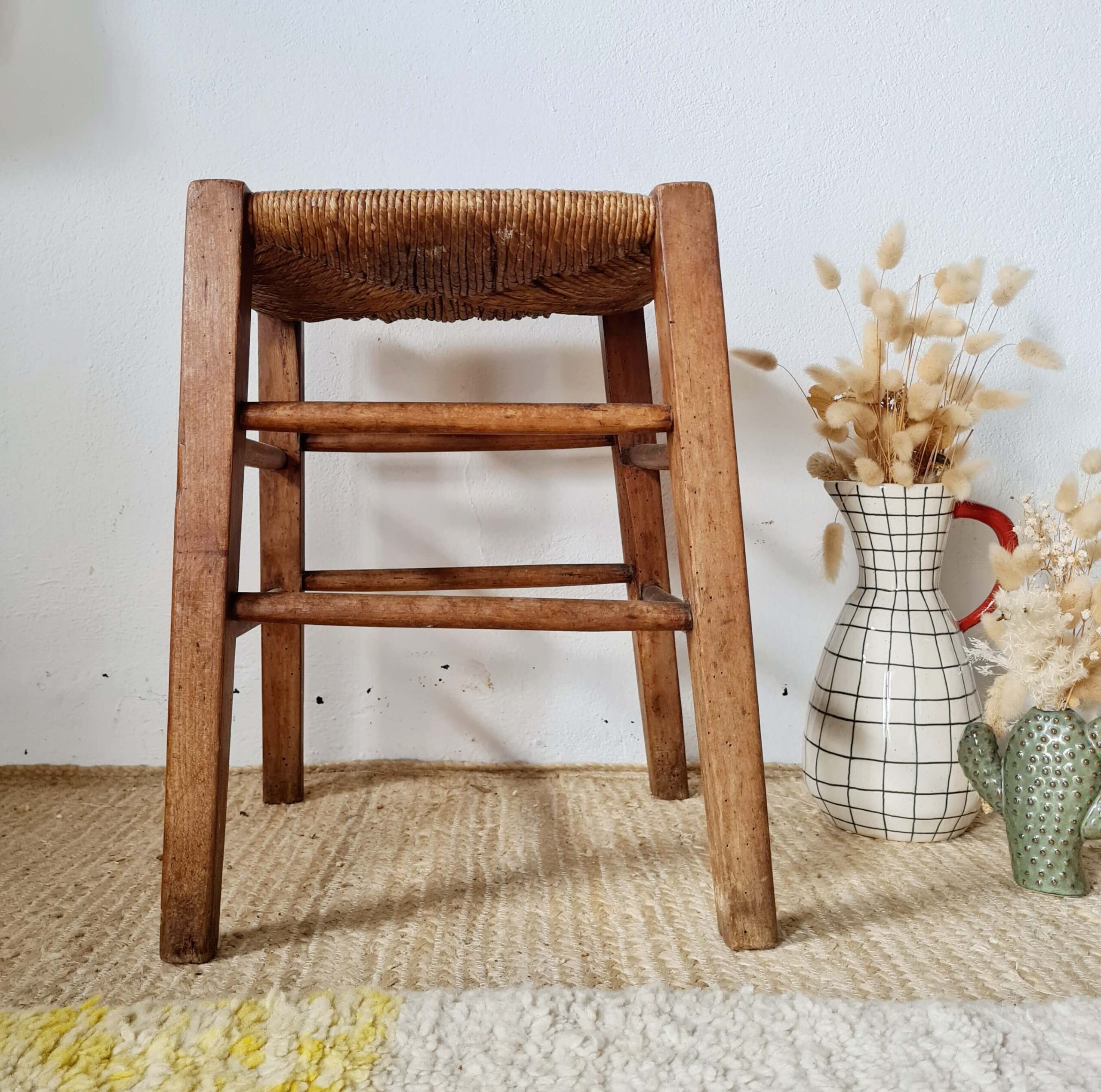 Tabouret rustique vintage en bois et assise en paille tressée à côté d'un vase.