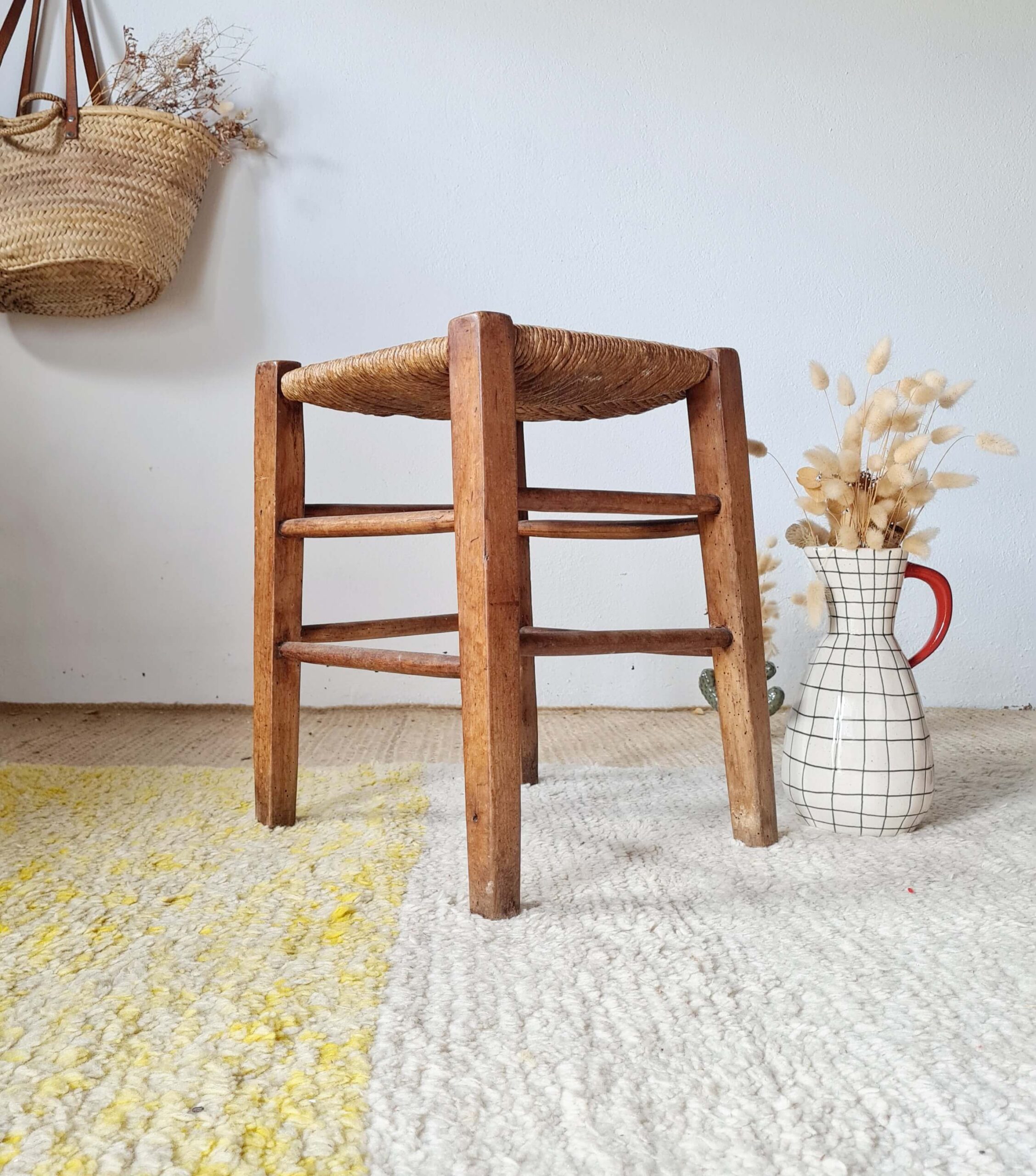 Tabouret ancien en bois et paille mis en scène dans un intérieur à la décoration bohème avec un panier en osier et des fleurs séchées.