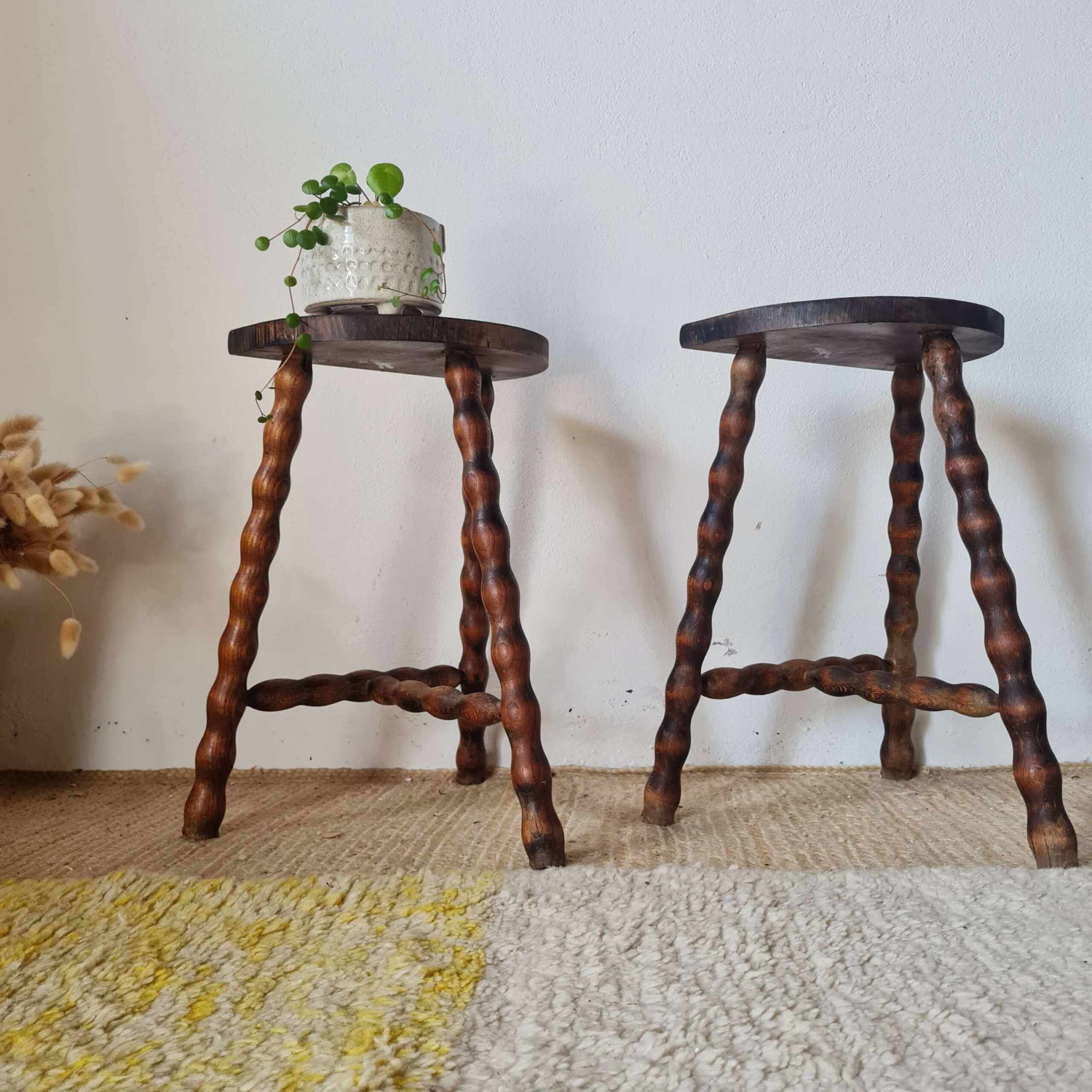Paire de tabourets vintage à trois pieds de style 'bobbin leg' (bois tourné en bobine) avec patine sombre, présentés de face