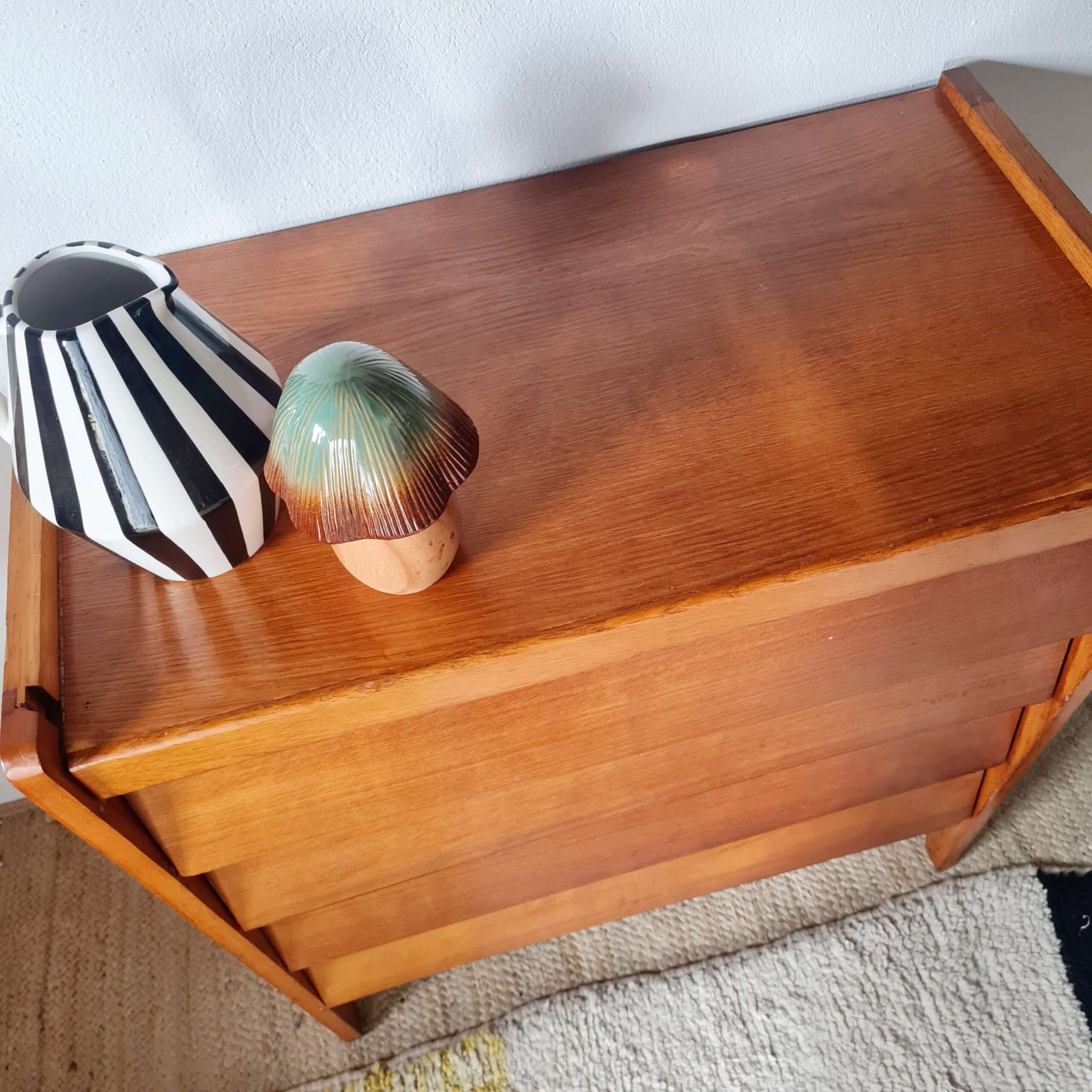Vue plongeante du plateau en bois vernis d'une commode vintage avec un pichet strié noir et blanc posé dessus.
