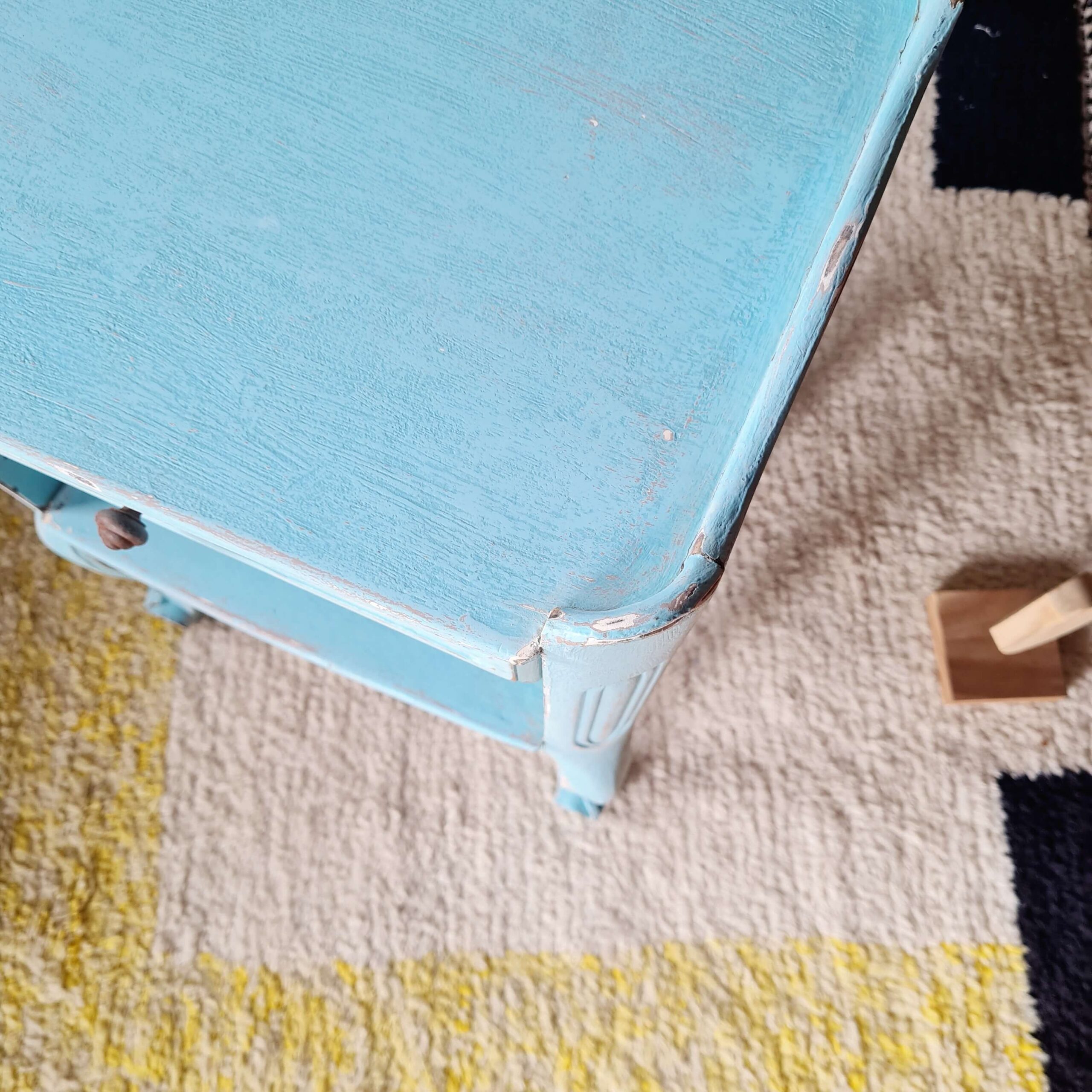 Zoom sur l'angle patiné et l'usure naturelle de la peinture sur le plateau en bois du meuble.